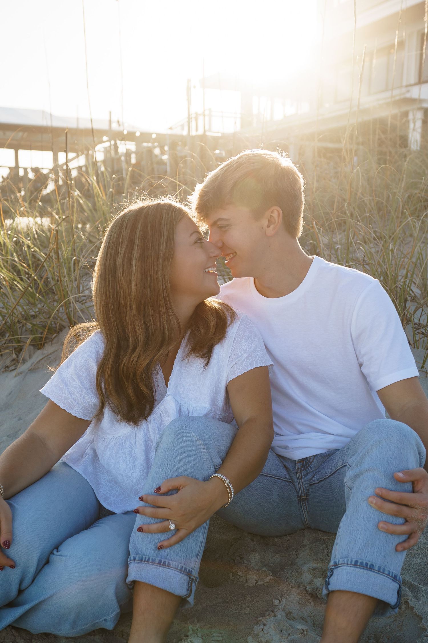 Couple sharing tender moments on beach dunes during golden hour sunset.