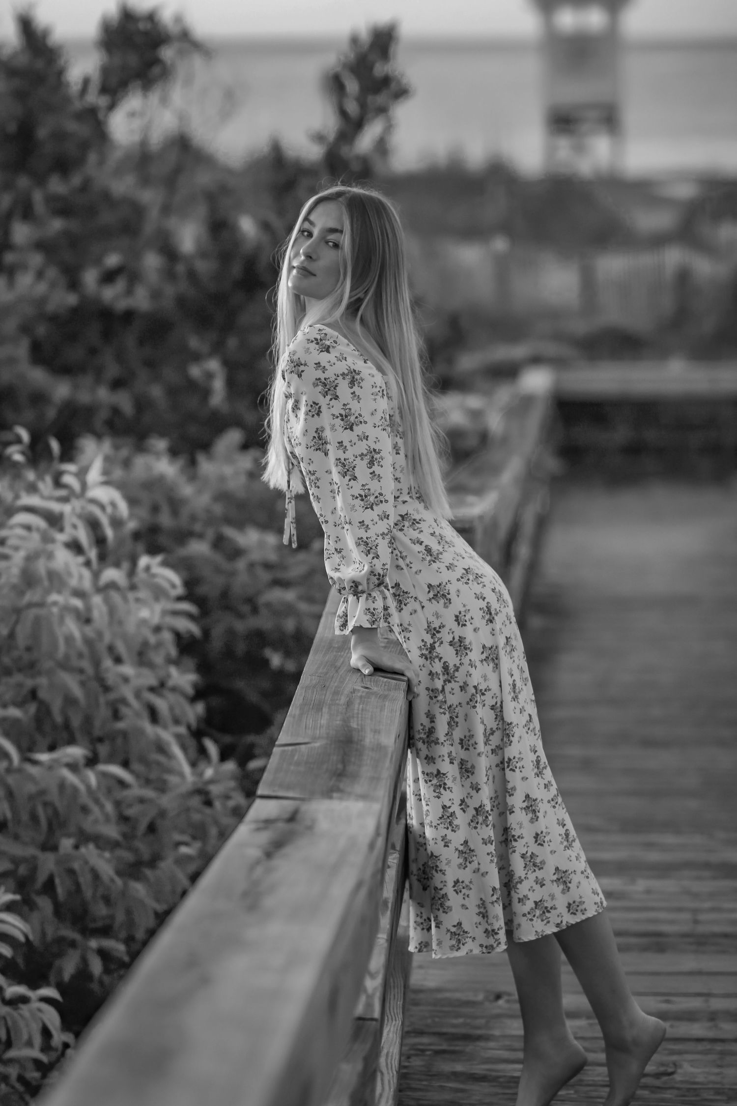 Black and white photos of someone in a floral dress posing on a wooden boardwalk.