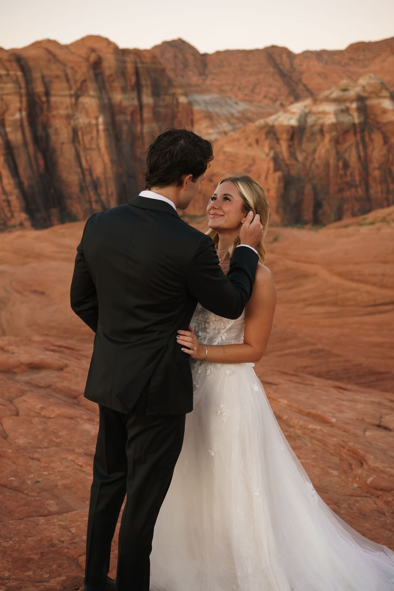 Wedding couple embracing against dramatic red rock formations in desert landscape.