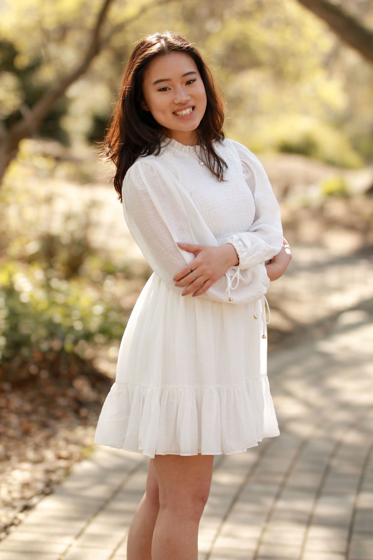 Person in white ruffled dress poses on garden path during golden hour.