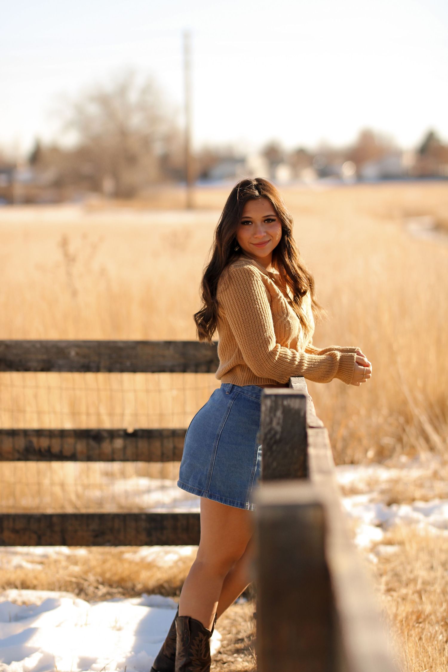 Winter fashion shoot by a wooden fence with tan sweater and denim shorts in golden light.