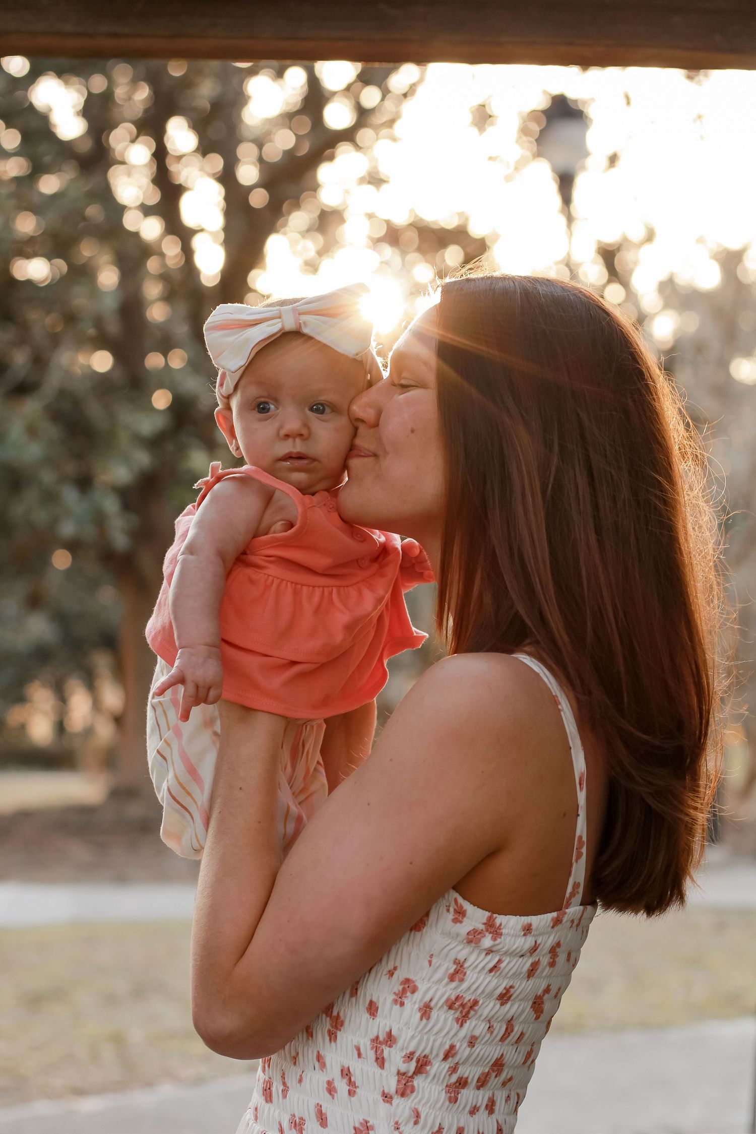 Parent sharing tender moment with baby in coral outfit during sunset photoshoot.