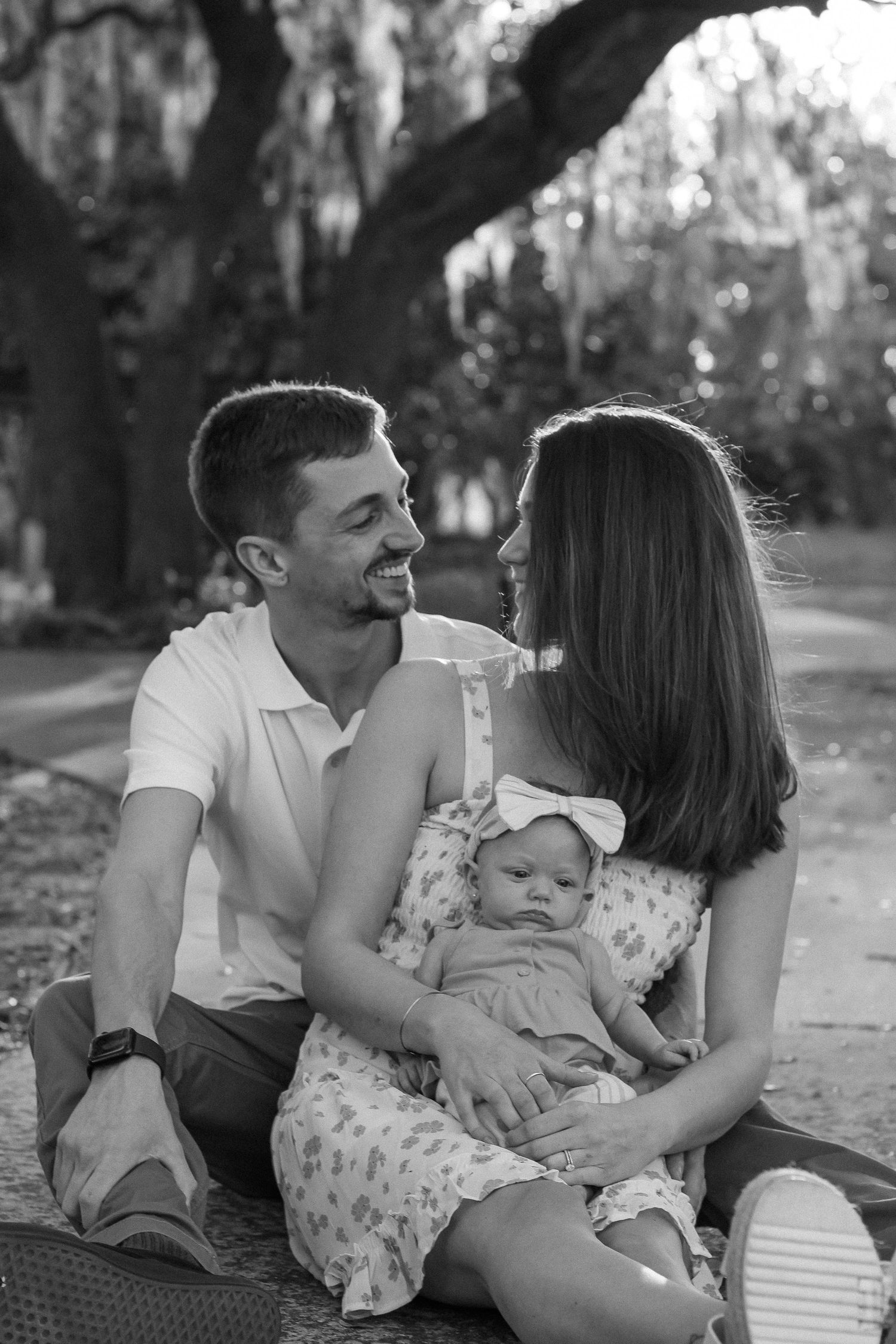 Outdoor family photo session showing intimate moments between parents and their baby under trees.