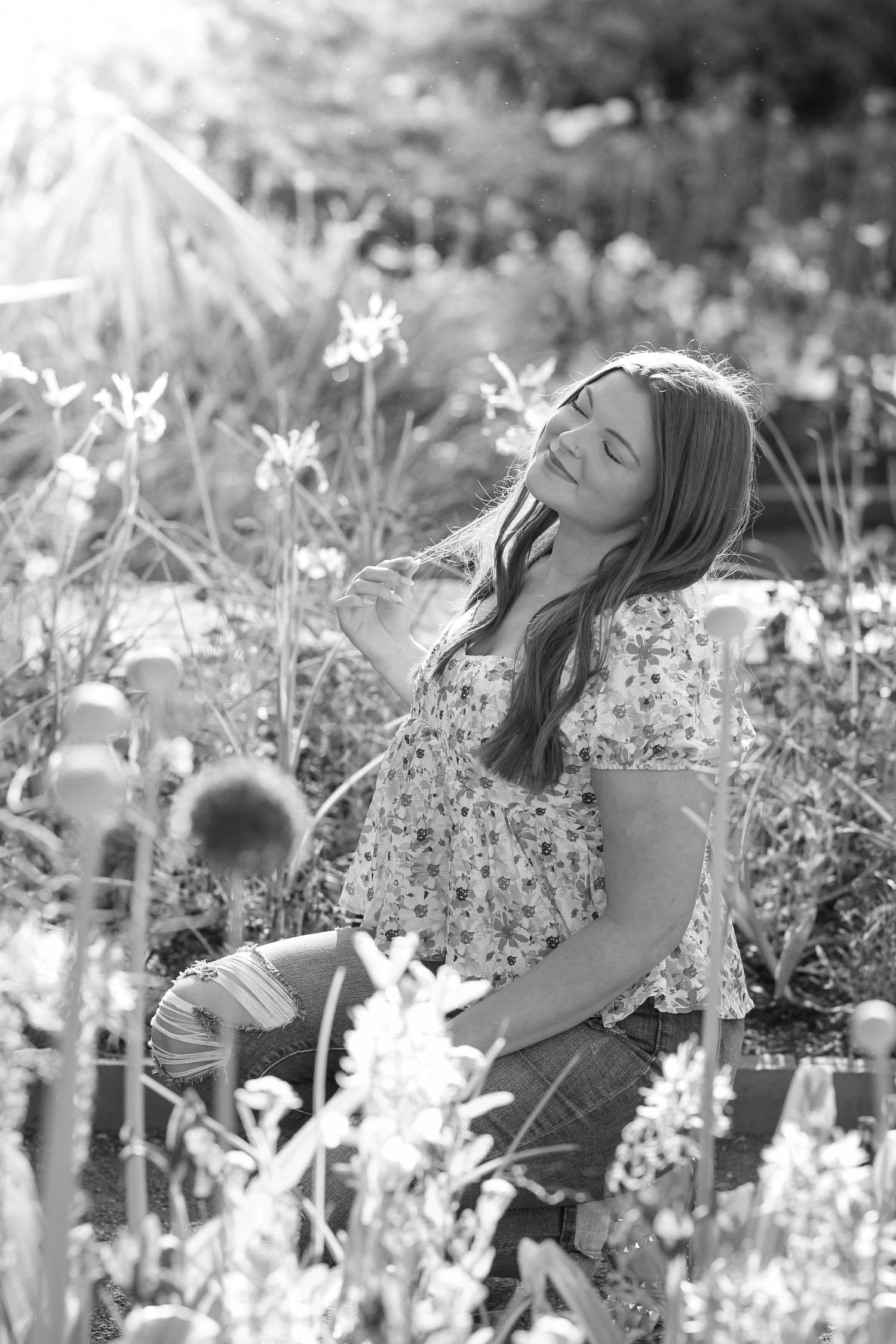 Graduate in floral dress poses among wildflowers in dreamy black and white photo.