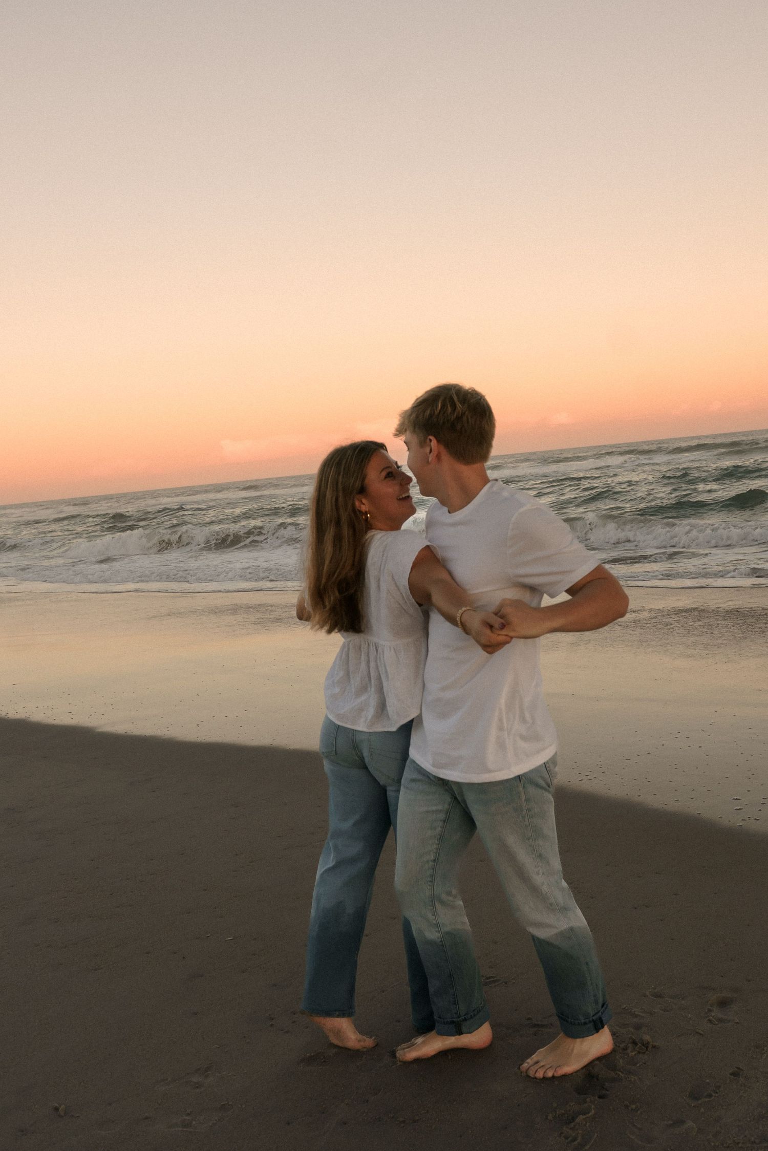 A romantic couple embracing on a sandy beach during golden hour.