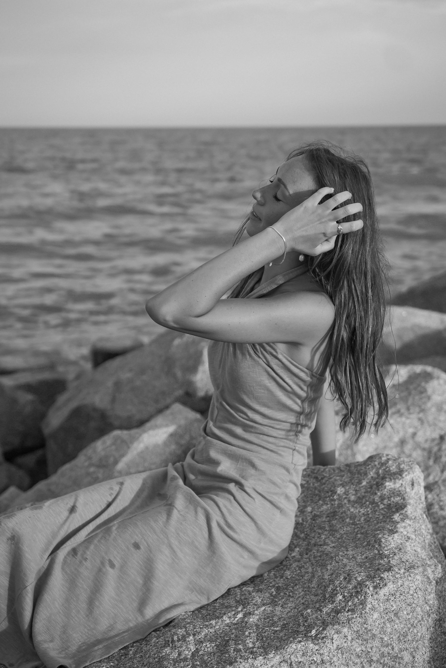 Black and white portrait of woman reclining on rocky beach overlook.