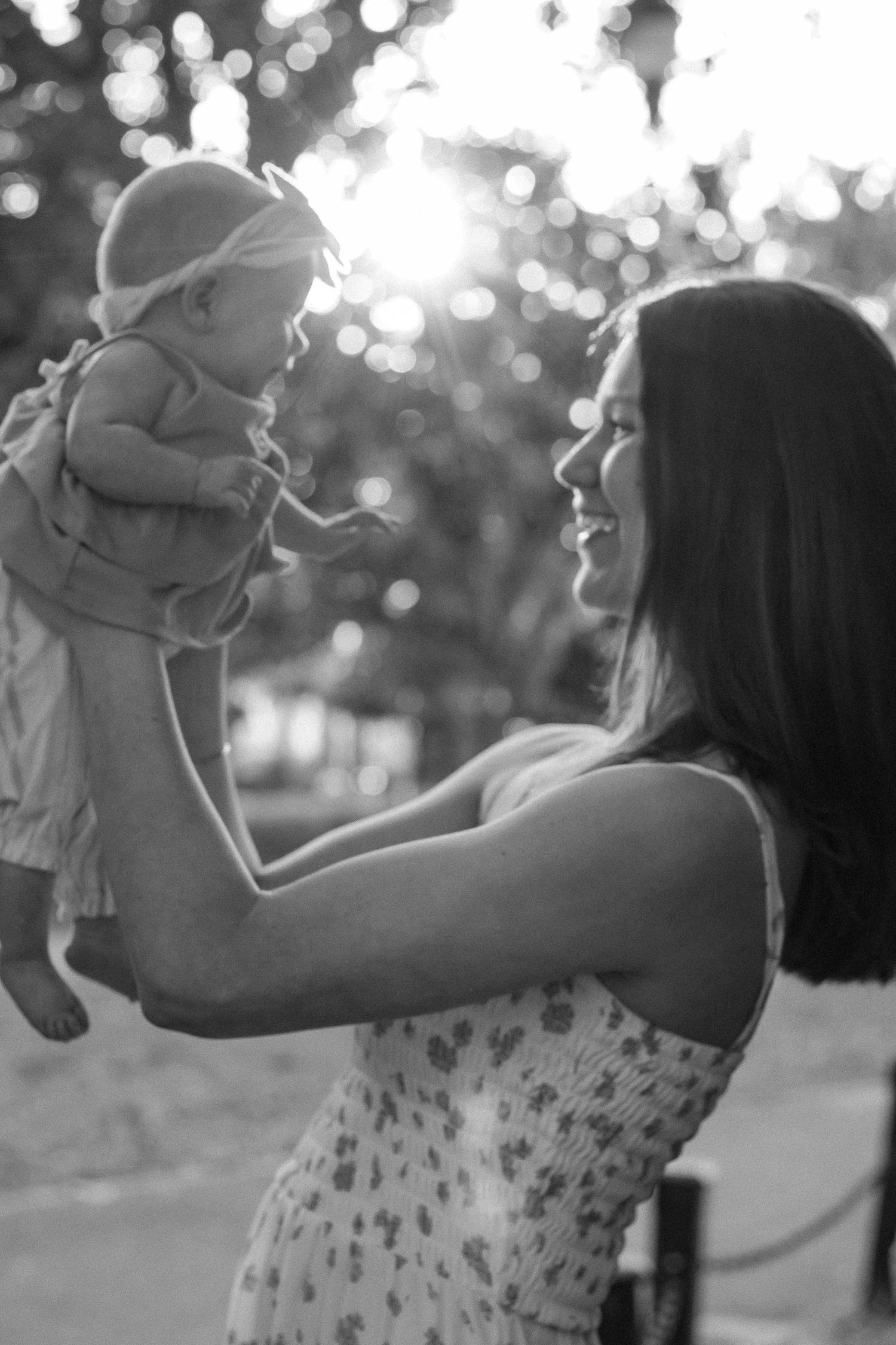 A tender black and white moment between parent and baby against sunlit bokeh background.