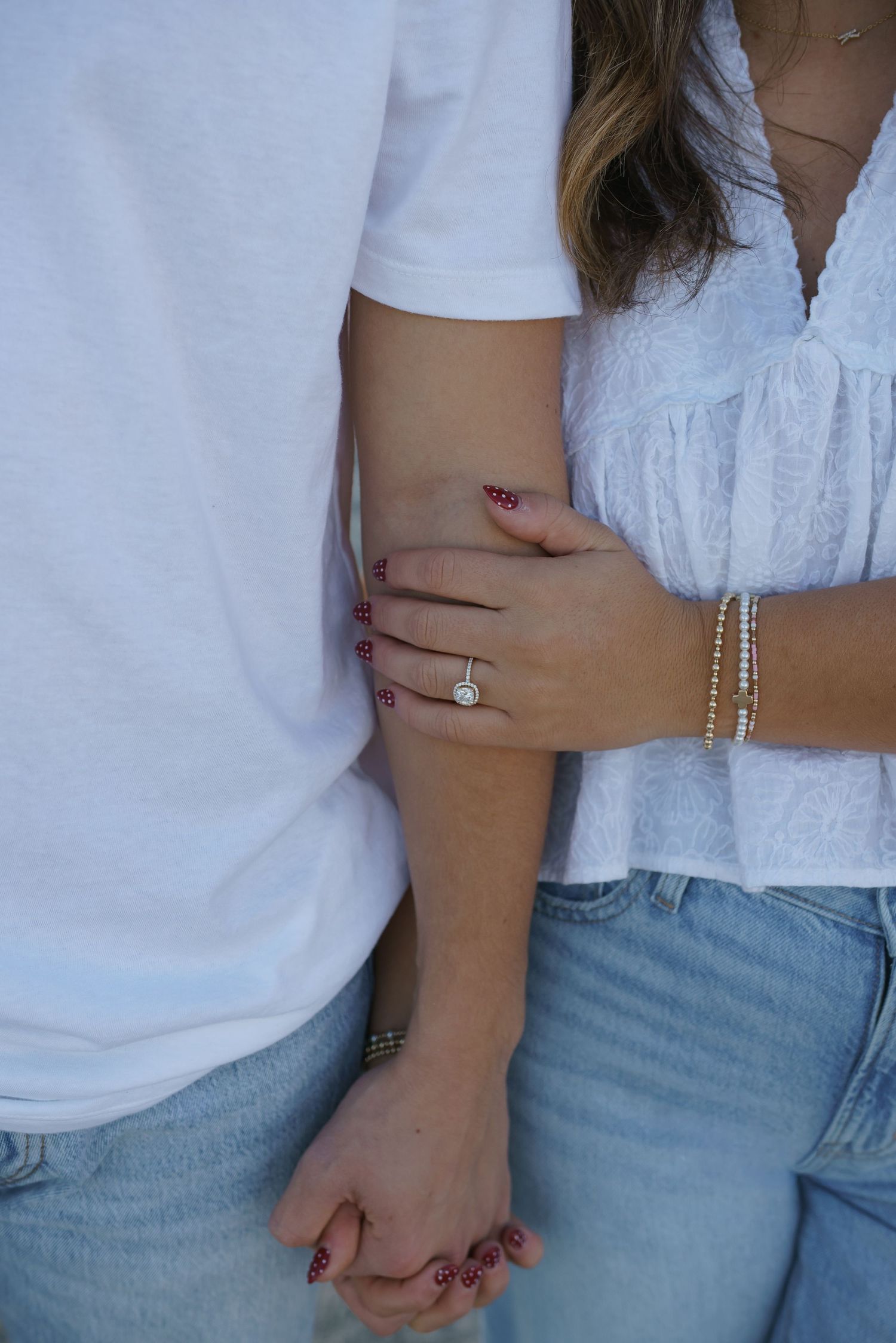 Close-up of couple's hands showing engagement ring and casual attire on beach.