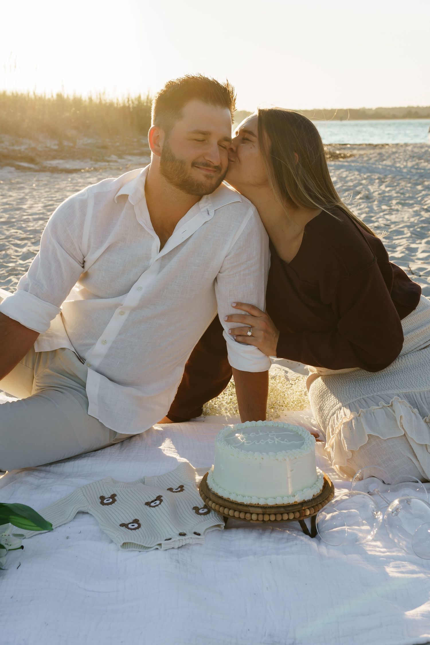 Romantic beach picnic scene with couple and celebration cake at sunset.