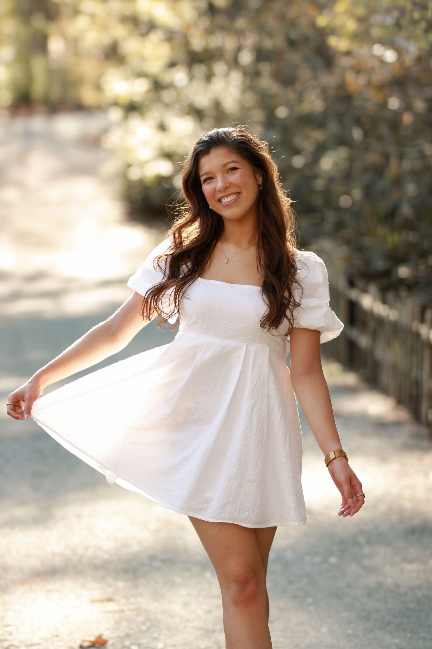 Person twirls in white dress with puff sleeves in sunny outdoor setting.