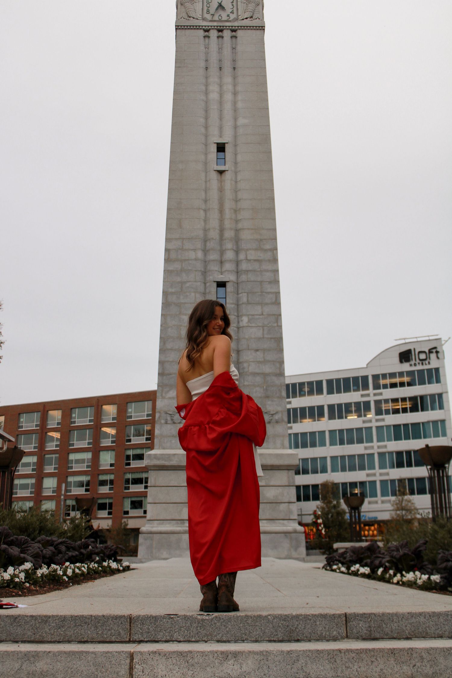 Person in red jacket poses dramatically in front of tall concrete monument structure.