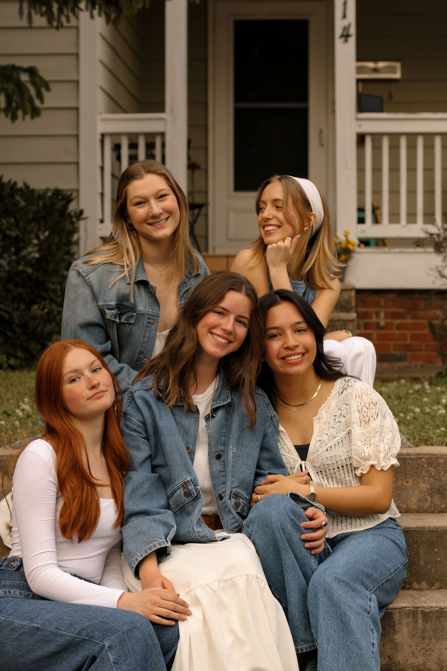 Five friends sitting on outdoor steps share joyful laughter while wearing casual denim and white outfits.