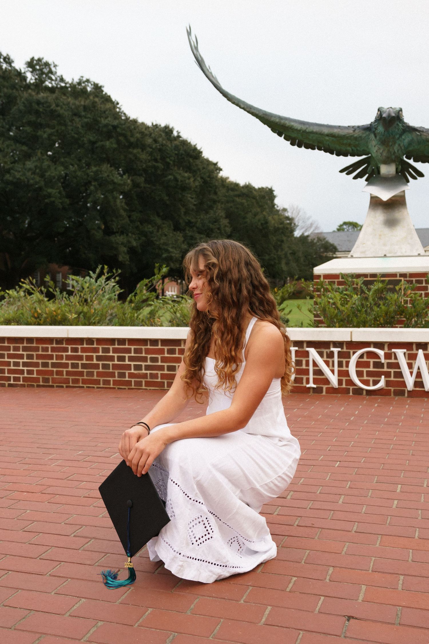 A graduate dodges a swooping hawk statue in a playful photo sequence at UNCW.