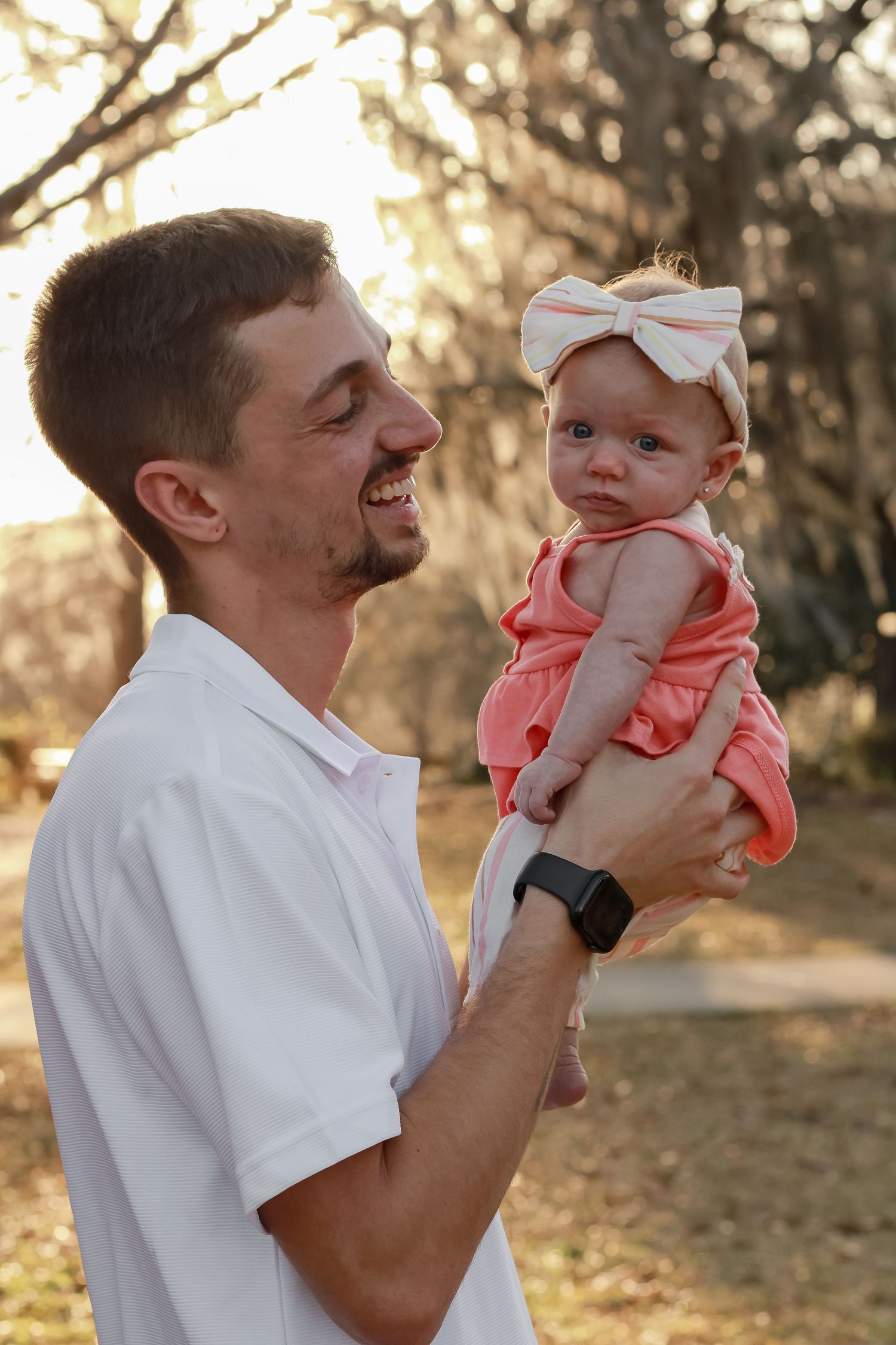 Sunset family photos showing tender moments between a parent and baby in coral-colored outfit.
