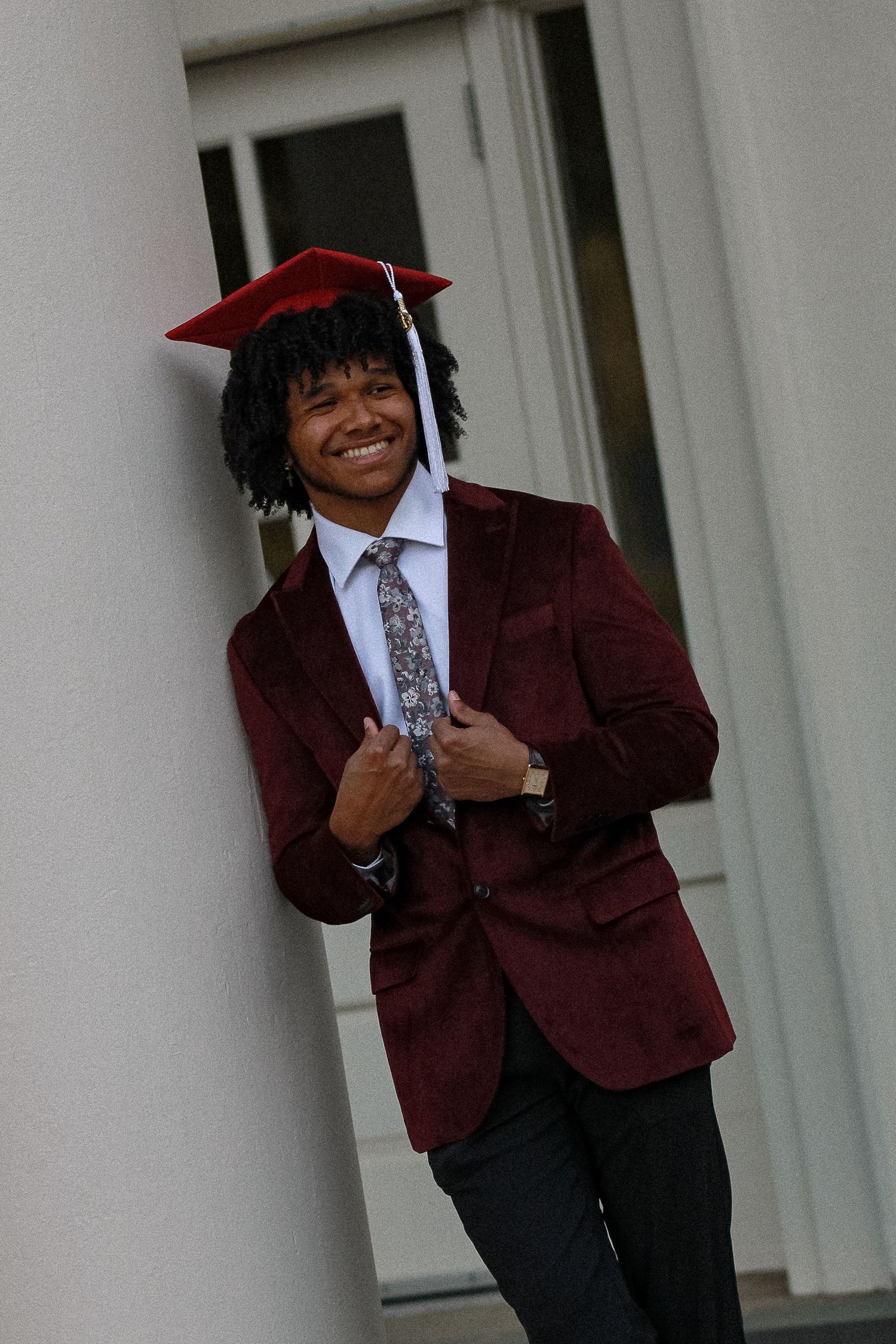 Graduate in maroon suit strikes dynamic poses near white pillars.