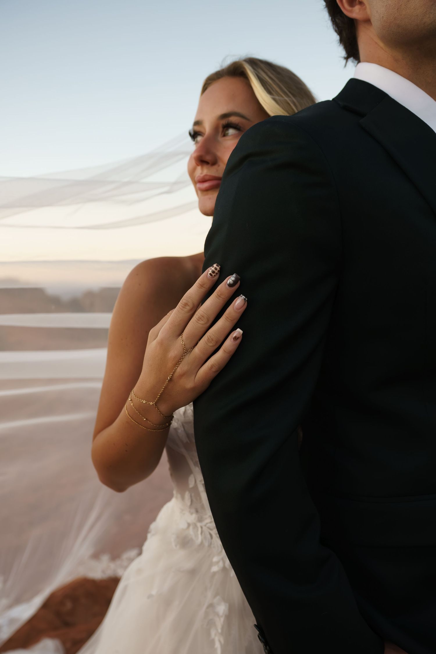 Elegant wedding couple embracing with flowing veil against desert landscape.