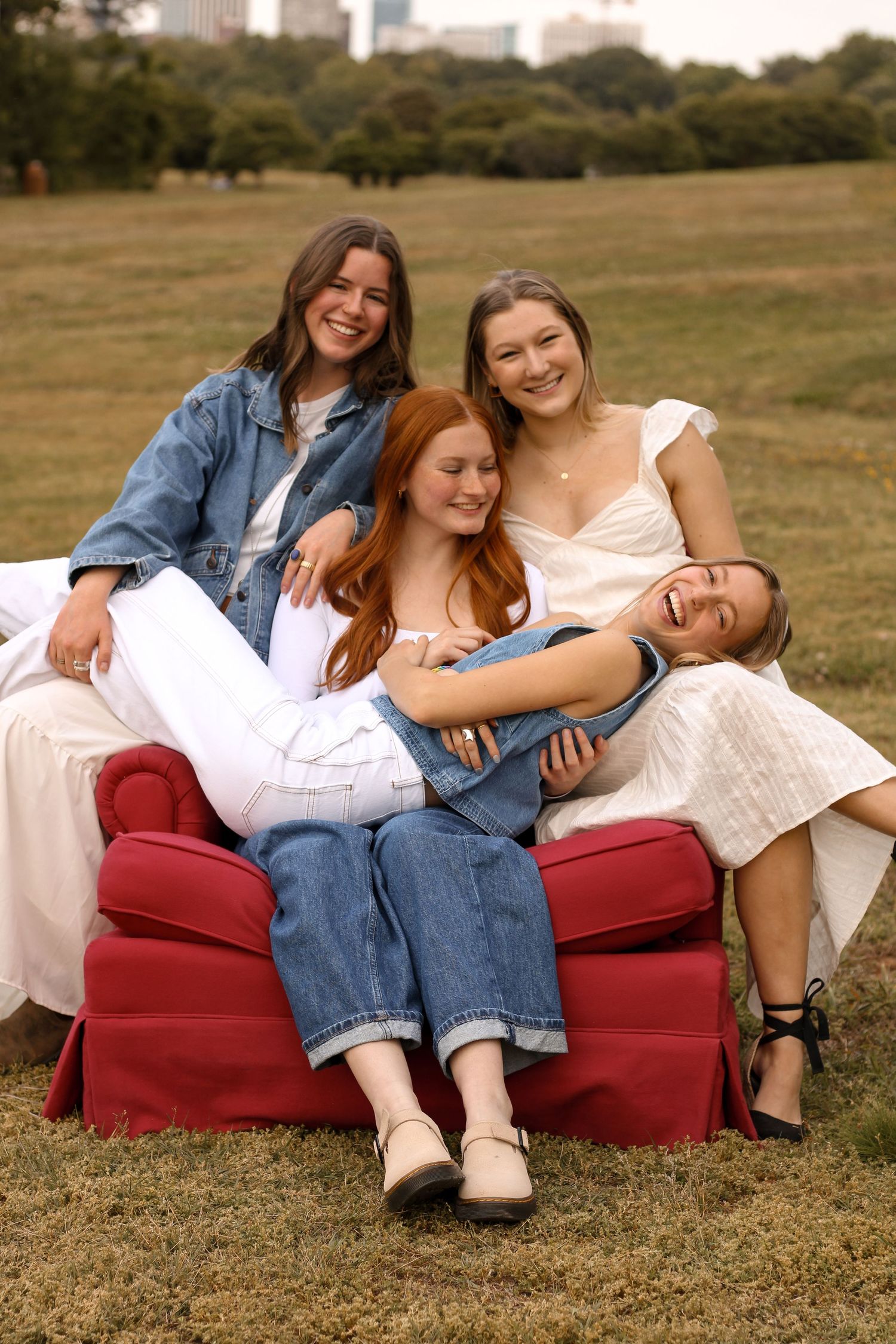Group relaxing on a red couch outdoors with urban skyline in the distance.