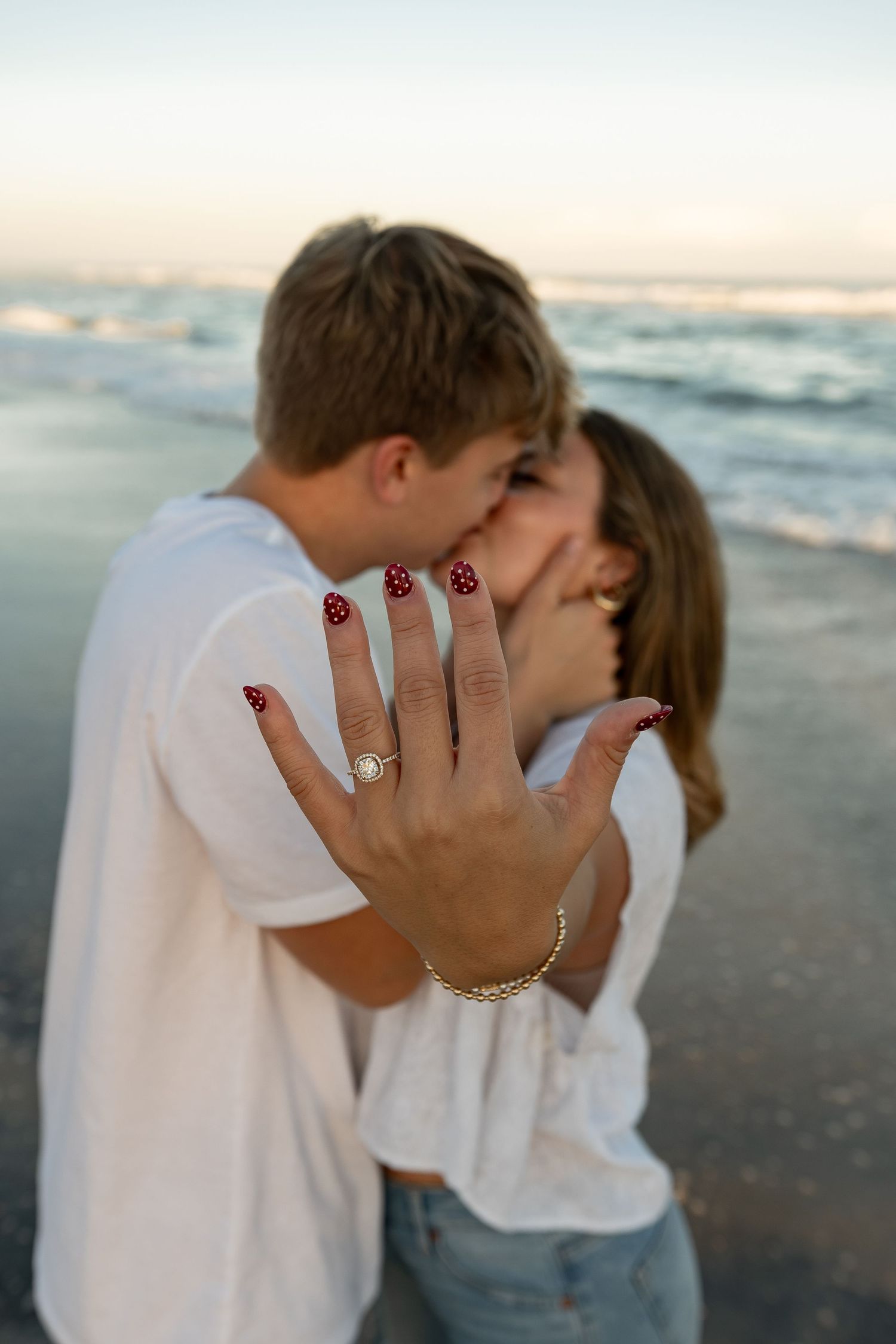Beach engagement photos showing close-up of couple kissing with engagement ring visible.