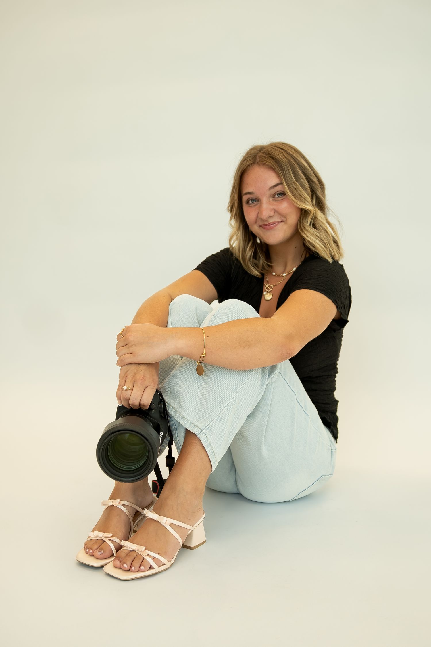 Casual portrait series in black top and light blue pants against white background.