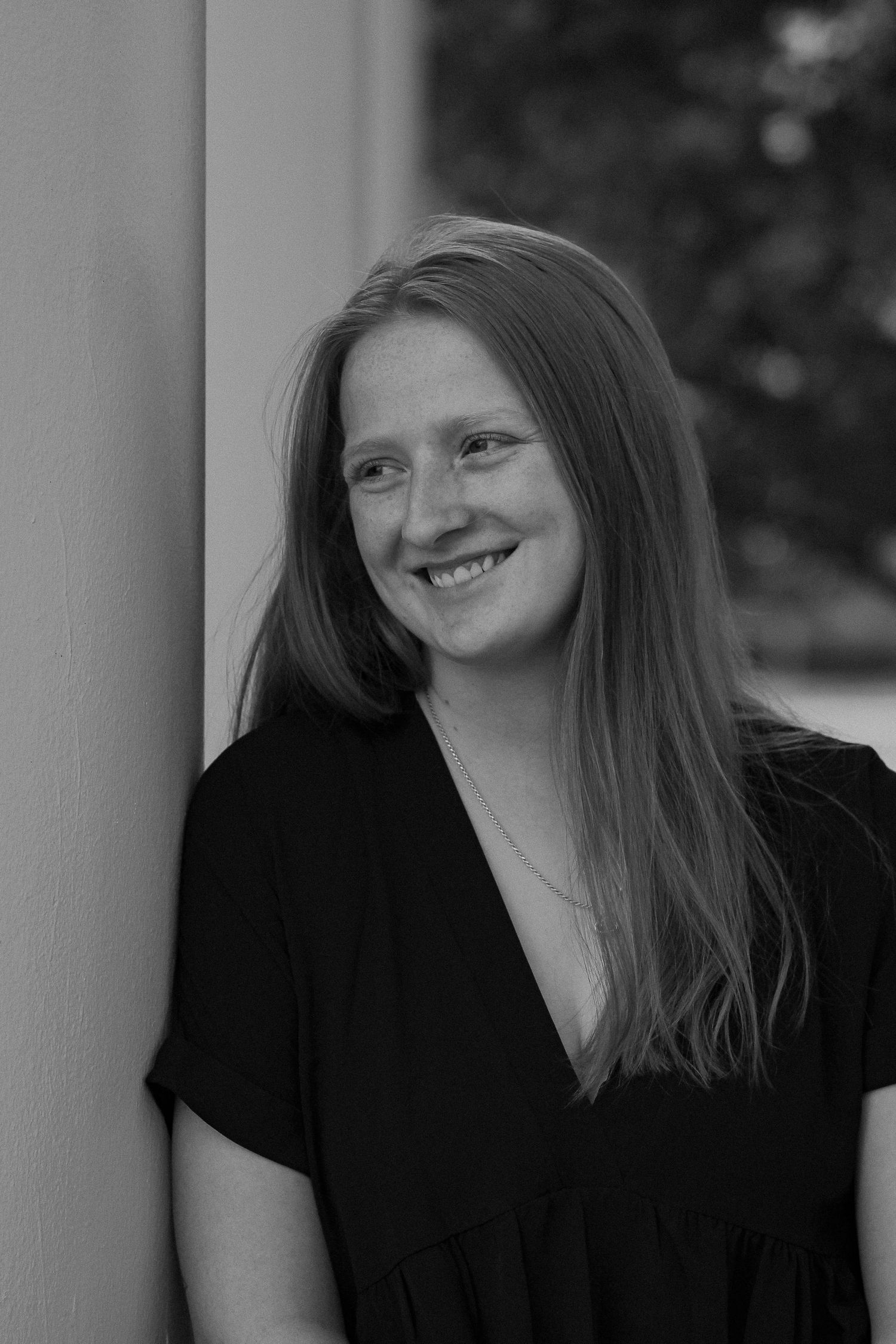Professional black and white portrait of a graduate in a black dress smiling warmly at the camera.