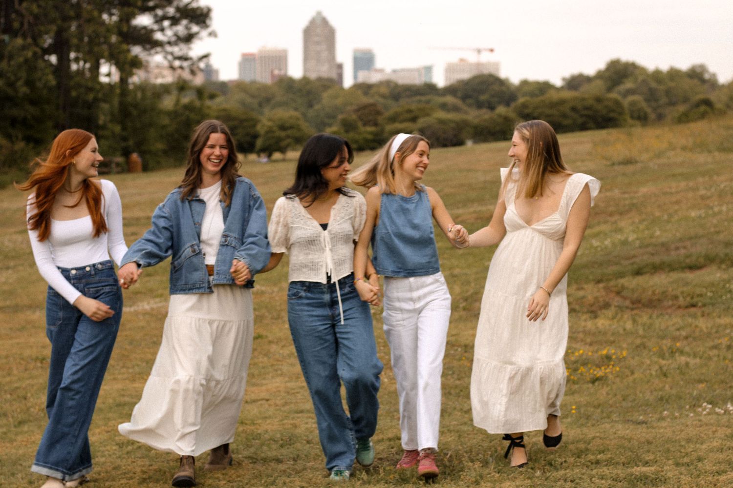 Group walking together in white dresses and denim through sunny field.