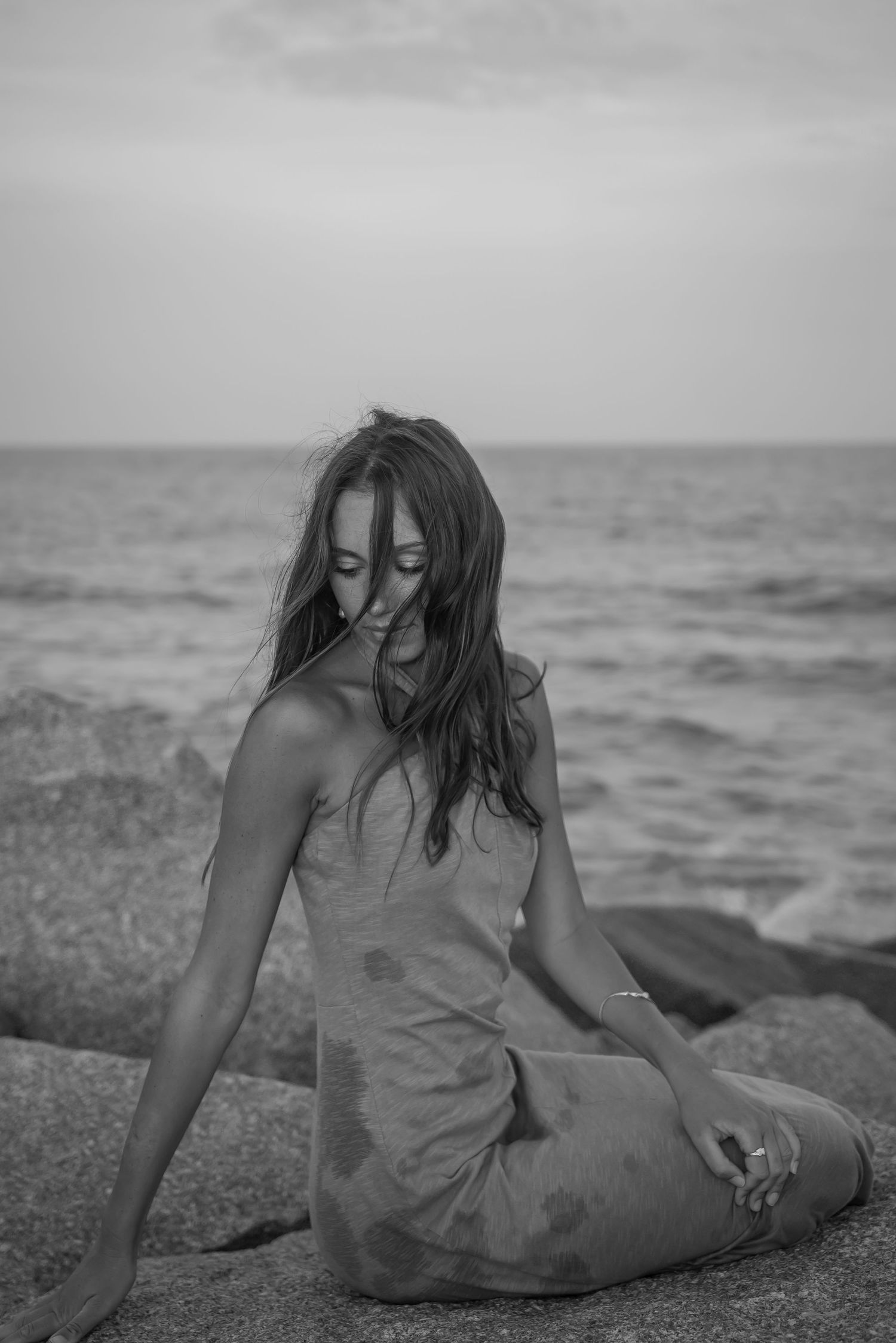 Artistic black and white sequence of woman lounging on coastal rocks by ocean.