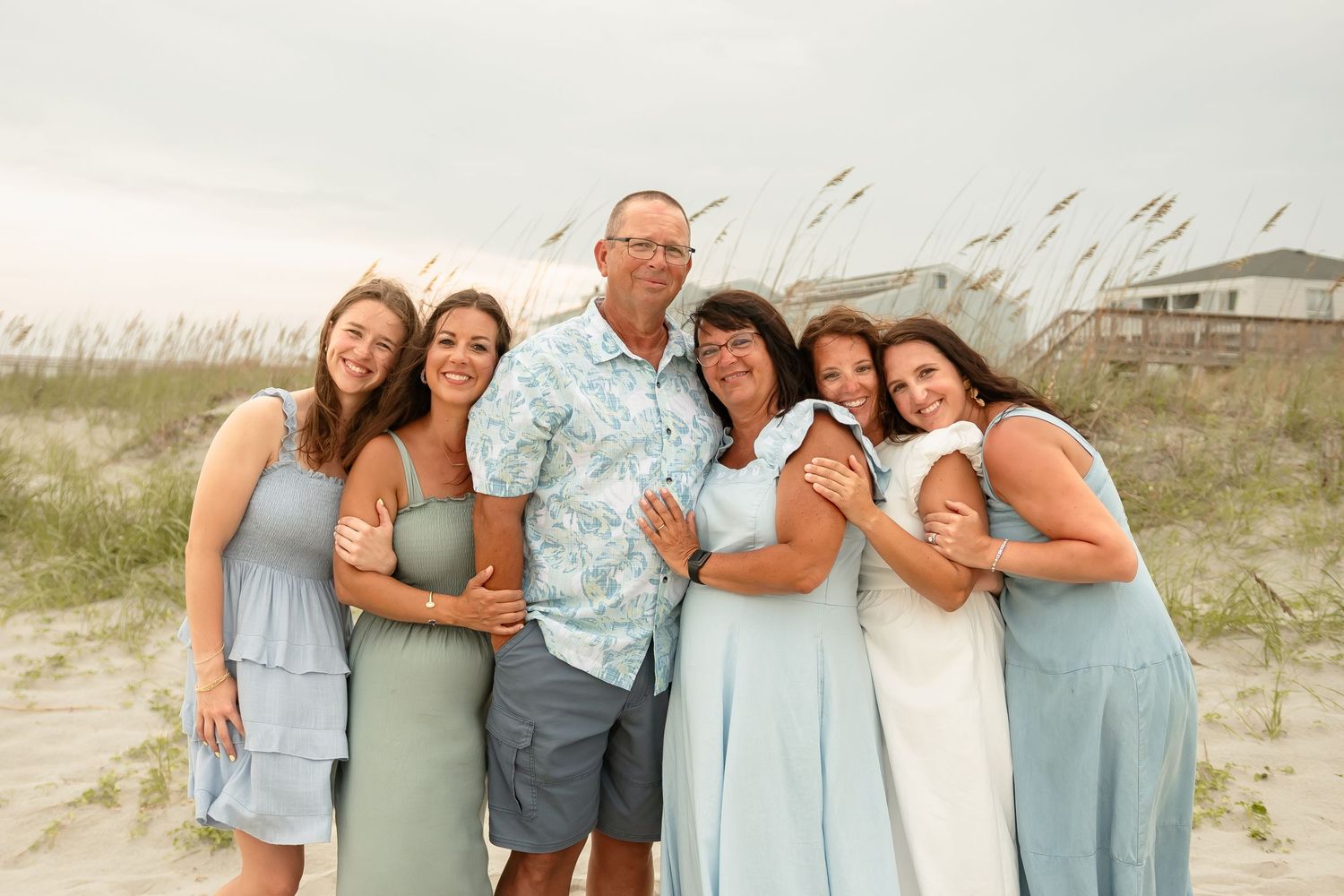 Family group photos in coordinating blue and green outfits on a beach with sea grass.