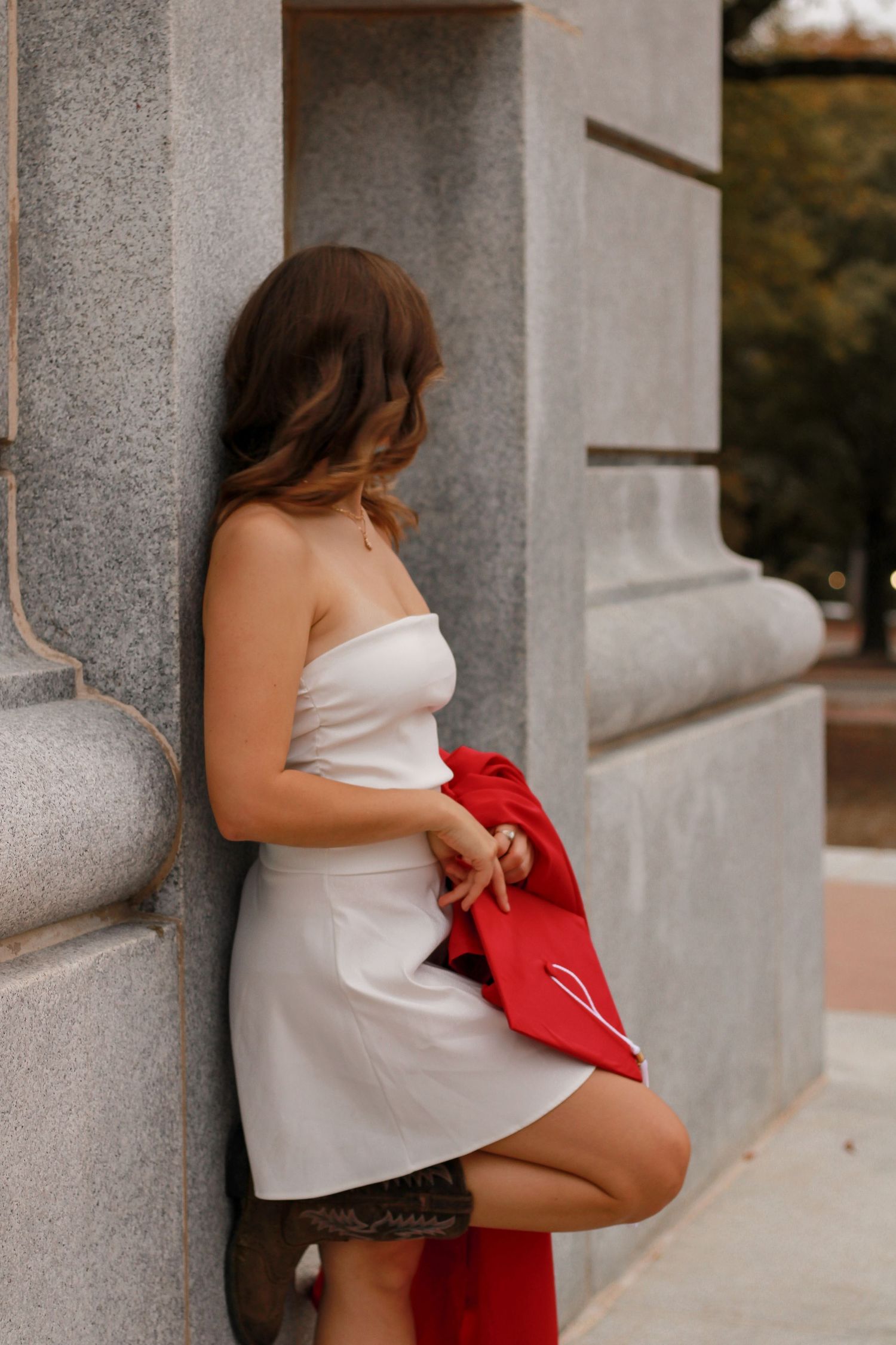 A person in white poses with a red jacket against concrete columns during a photoshoot.
