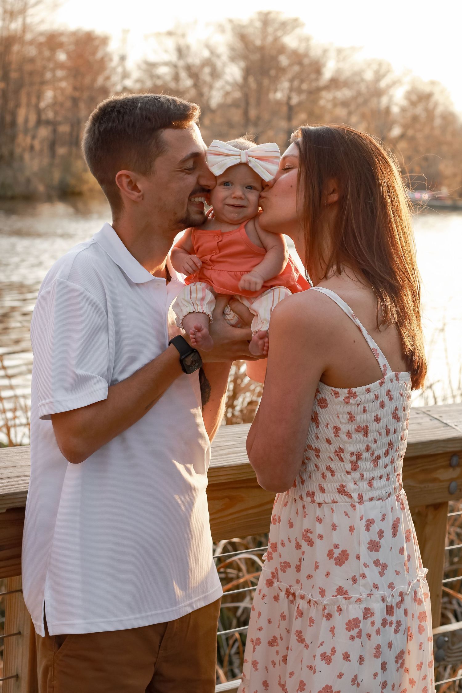 A loving family shares tender moments with their baby in coral dress during golden hour.