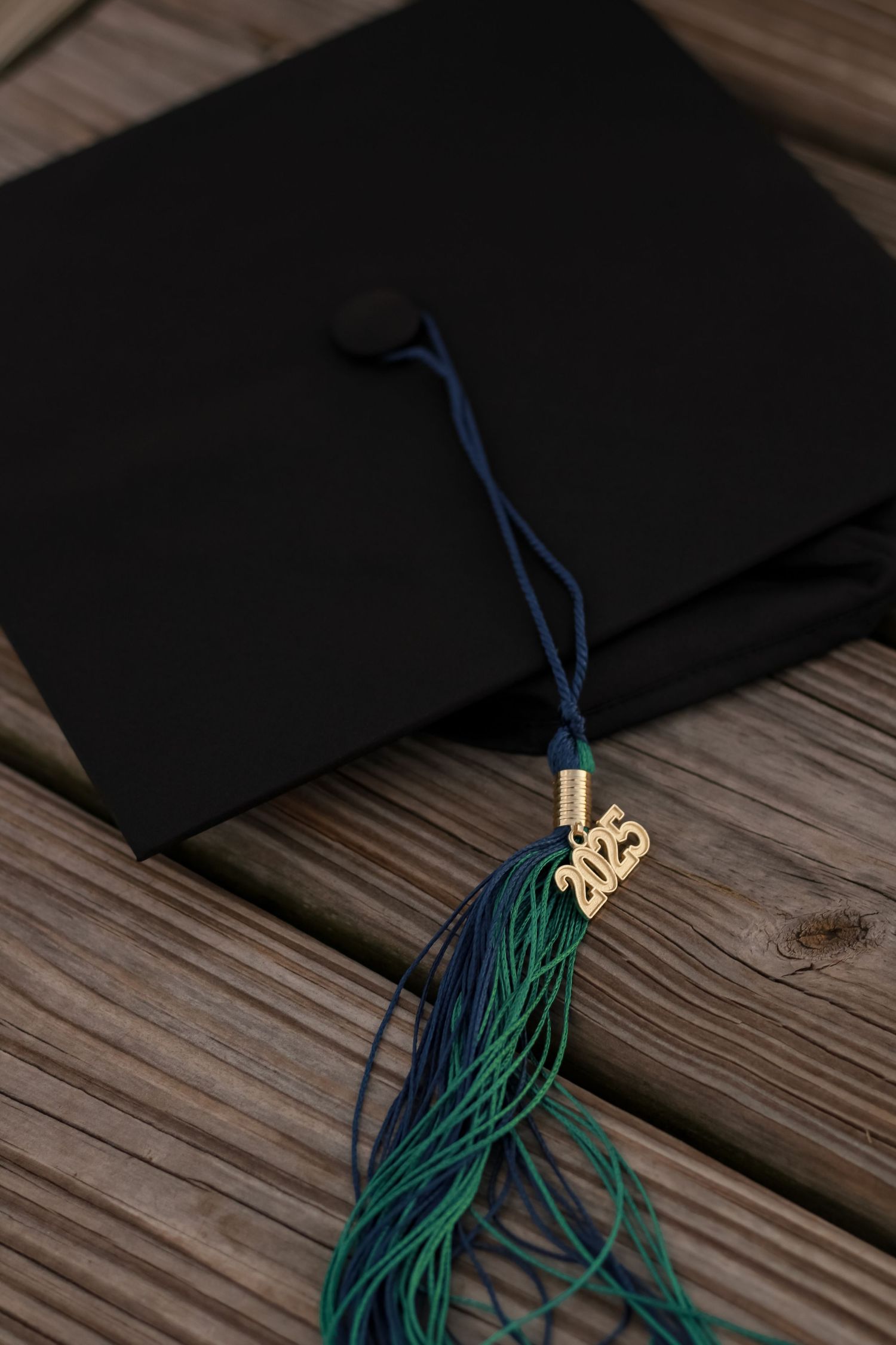Graduation tassel and cap on wooden deck with dark moody lighting.