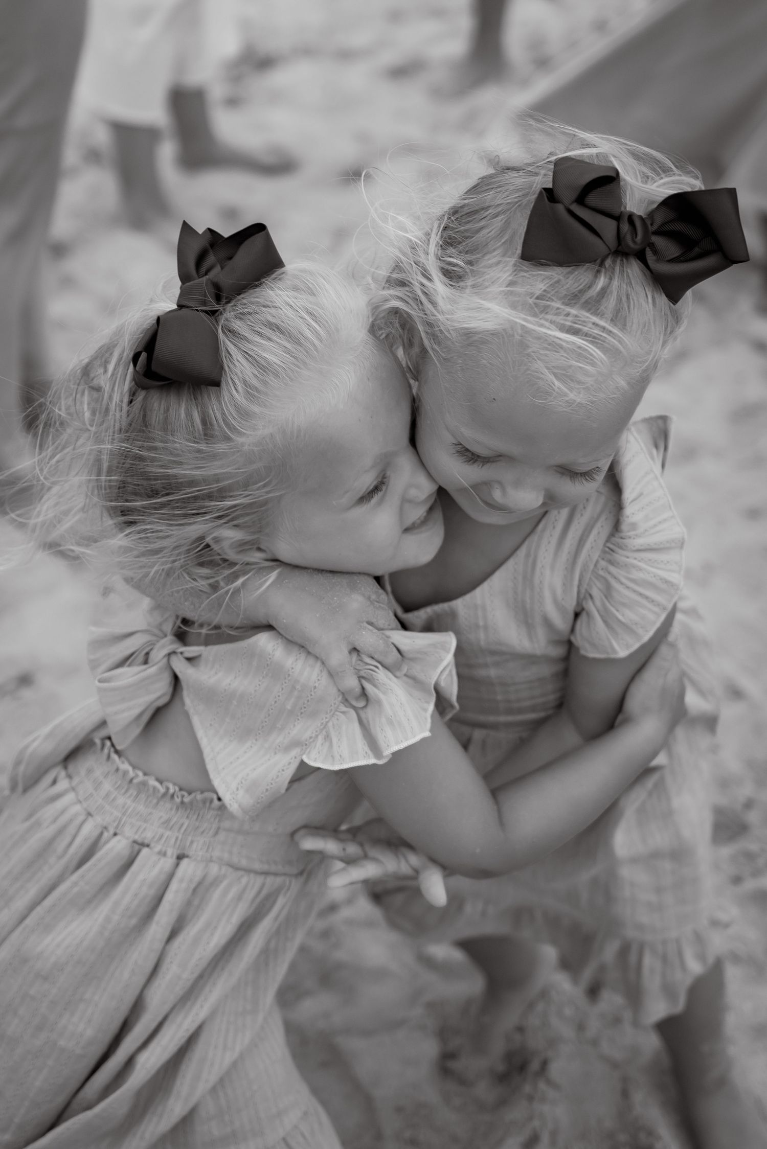 Black and white series of two young children in vintage dresses sharing sweet moments on the beach.