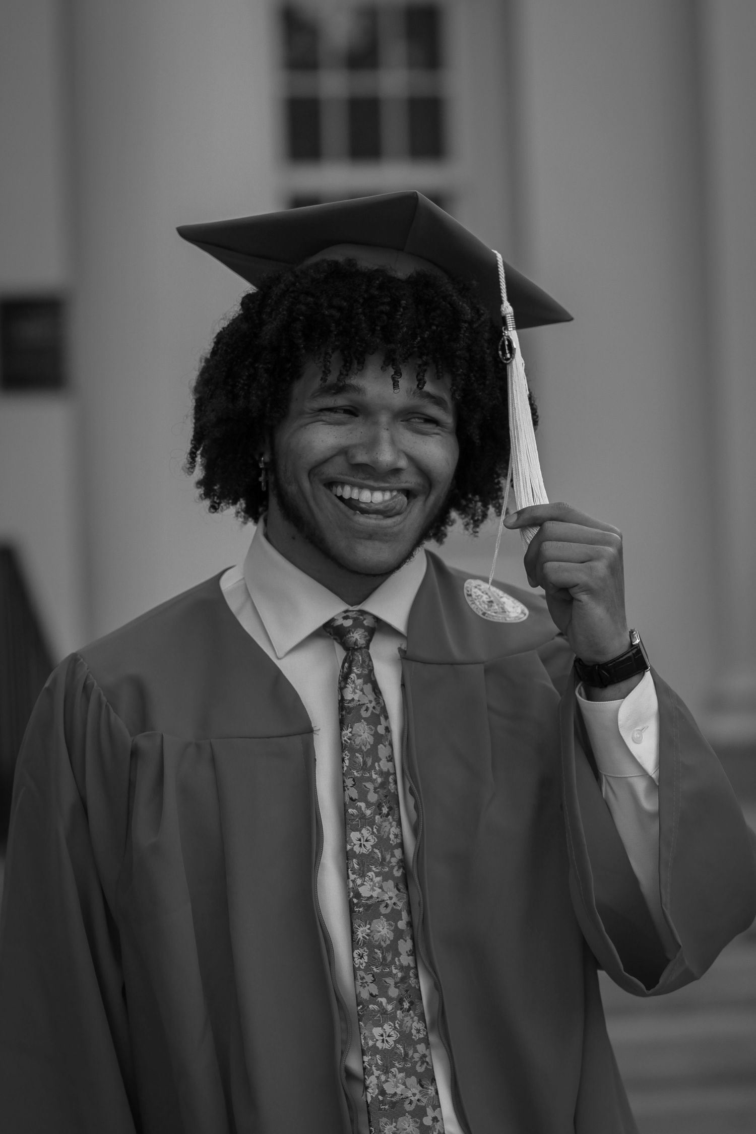 Graduate in cap and gown smiling while holding tassel.