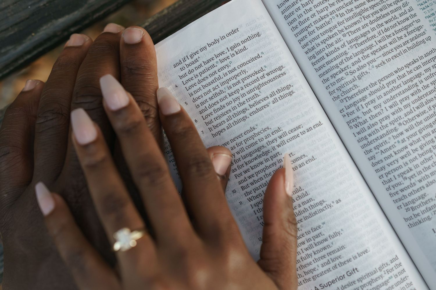 Close-up of hands with manicured nails resting on an open book or scripture.