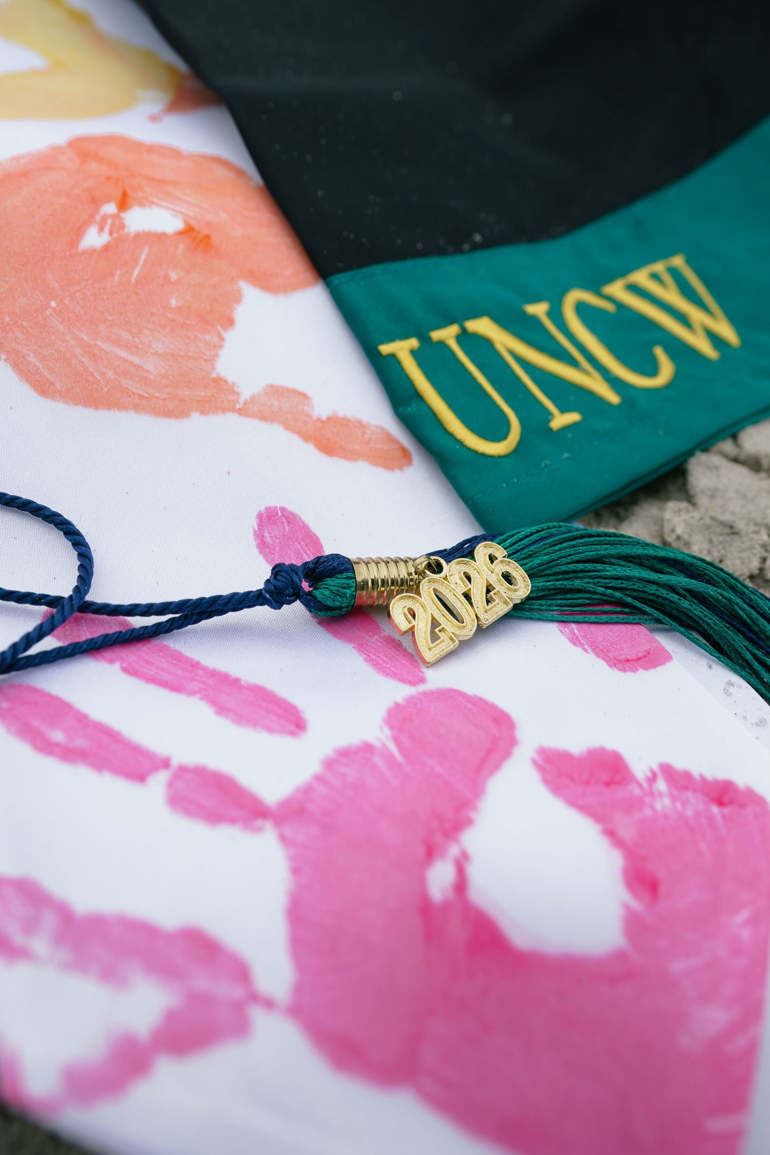 UNCW 2020 graduation cap with green tassel and gold charm on handprint artwork.