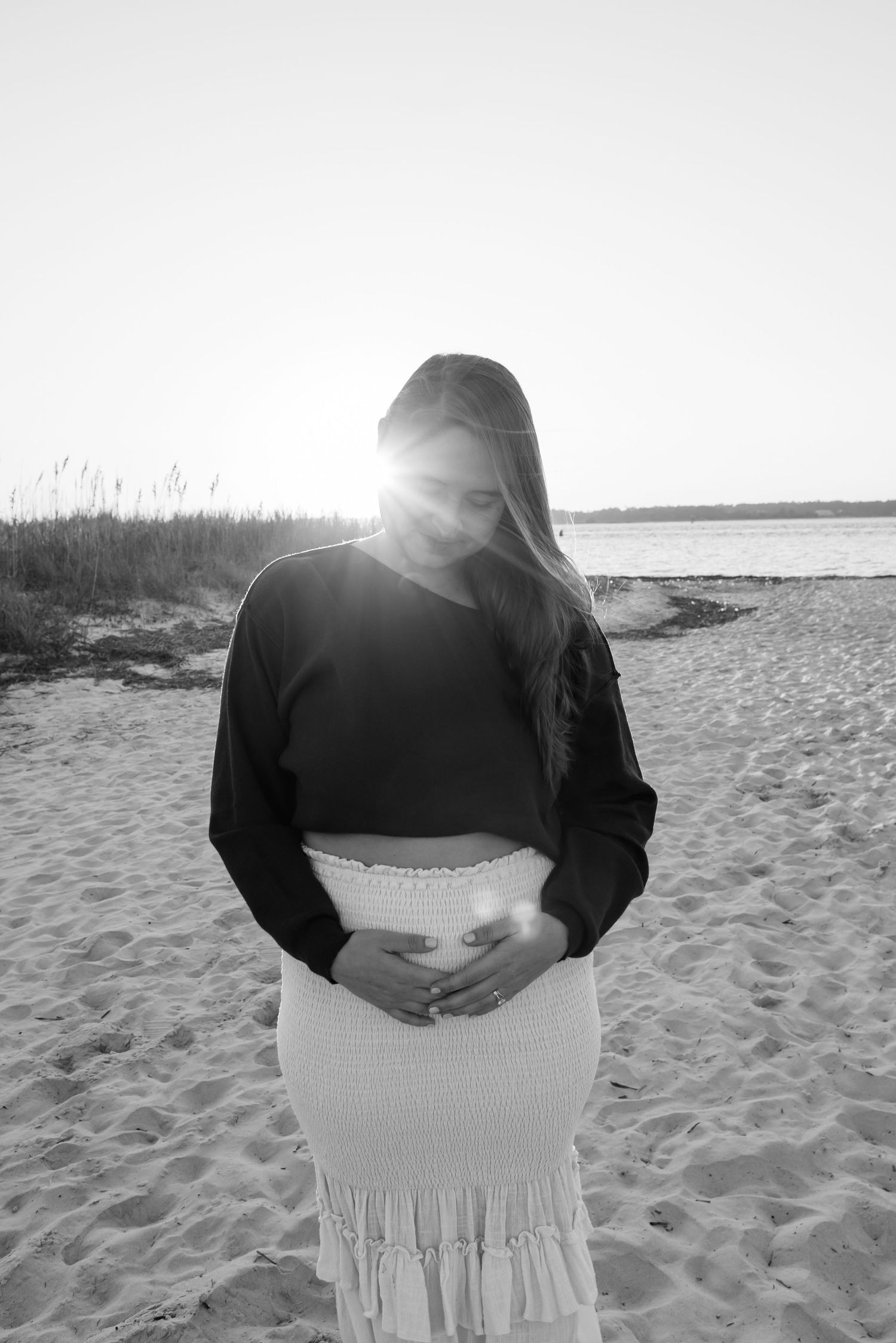 Silhouette against sunset on beach wearing cropped sweater and white skirt.