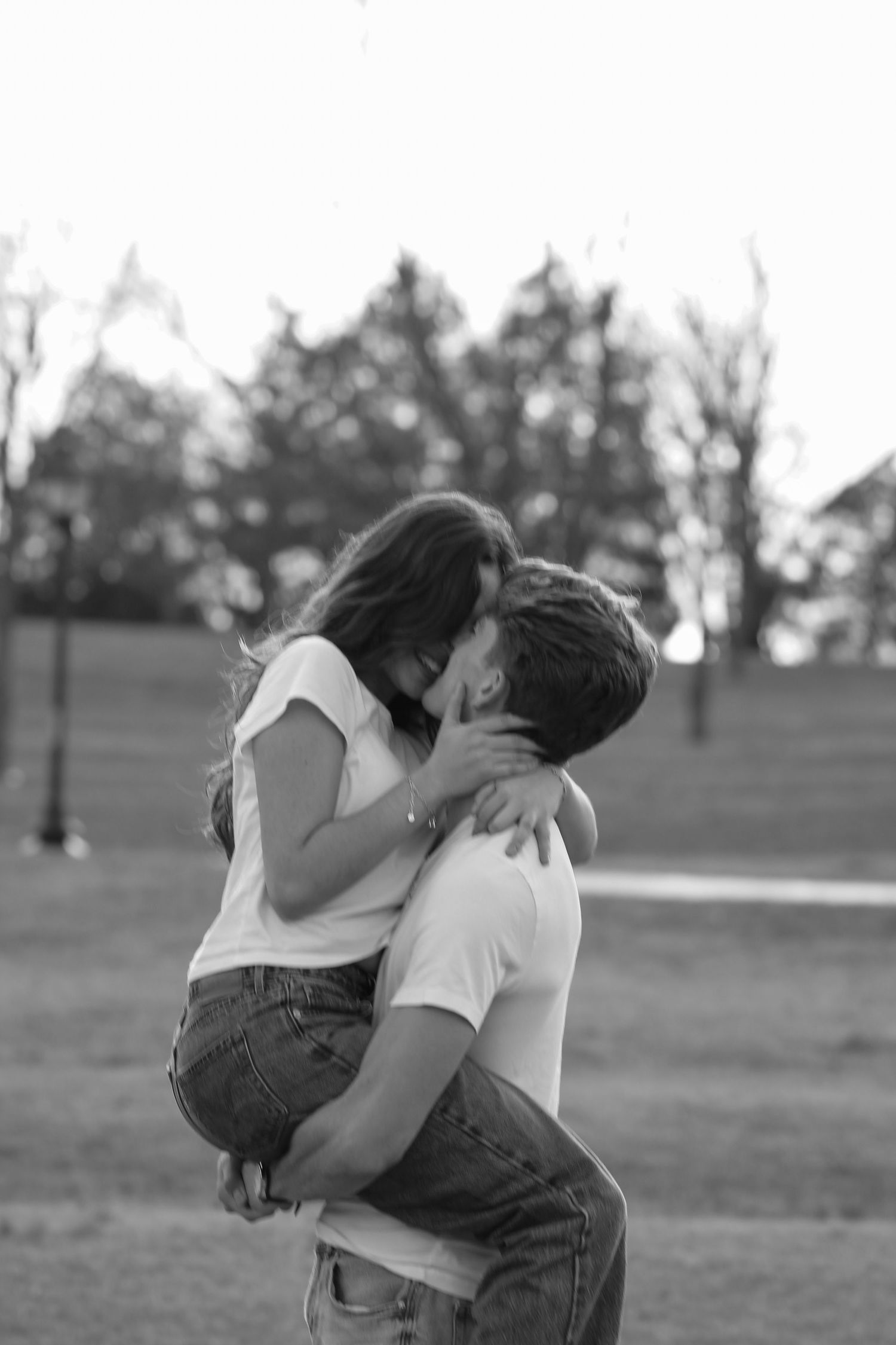 A romantic embrace captured in a park setting during daytime.