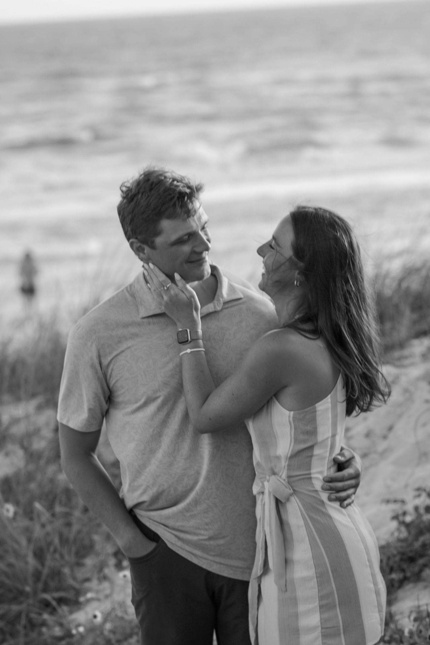 Couple embracing on beach dunes in black and white photography.