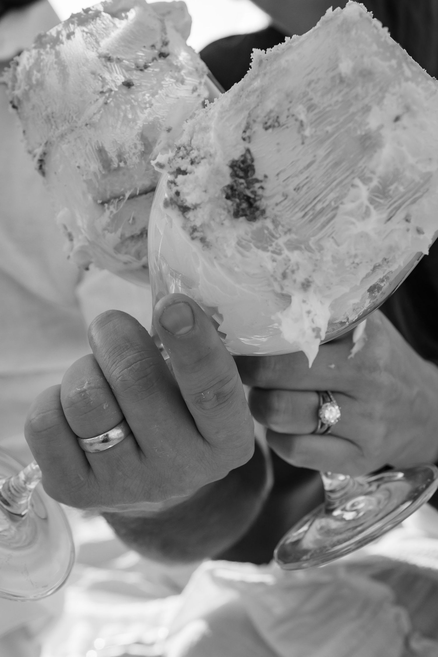 Black and white photo of hands holding desserts with engagement rings visible.