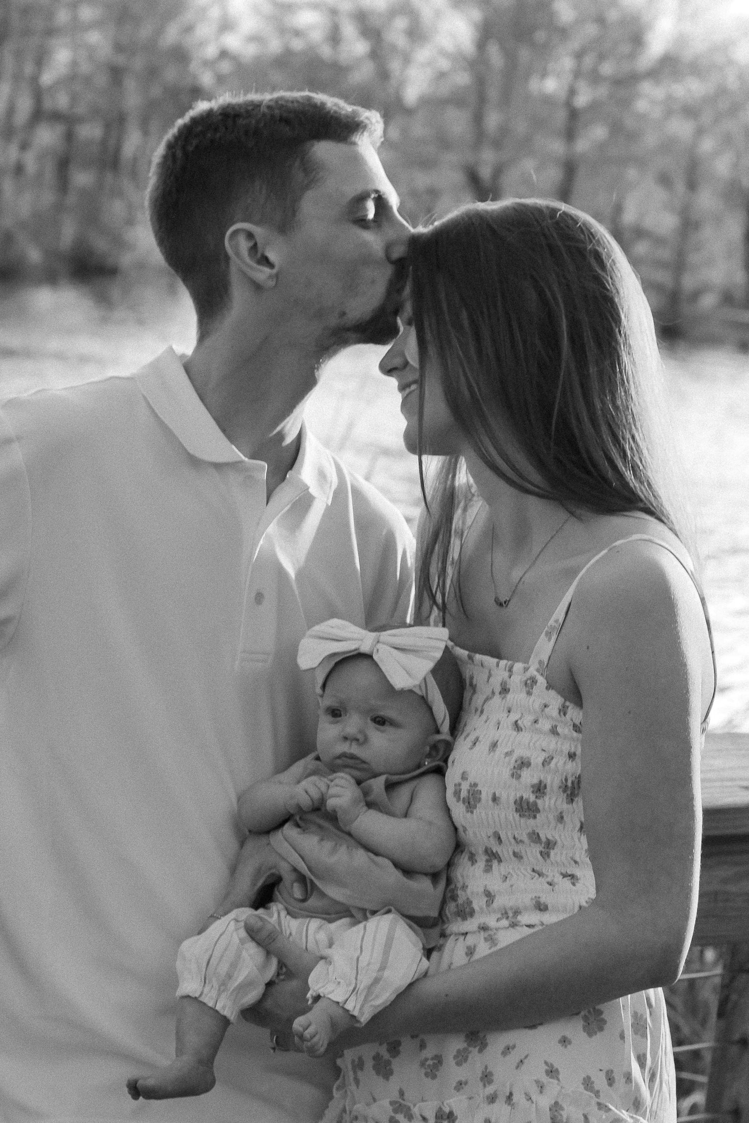 A black and white family portrait showing tender affection while holding their baby.