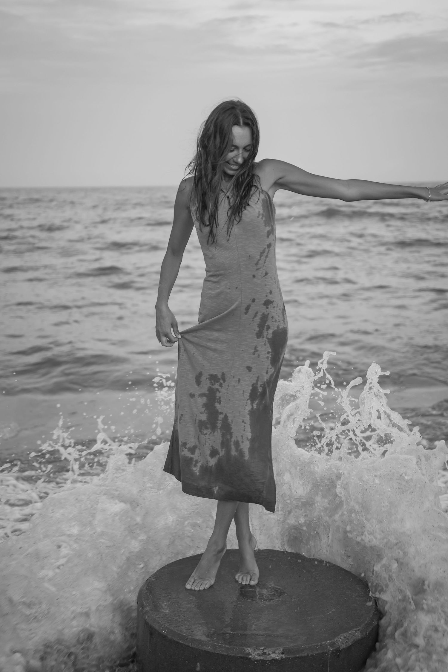 A sequence of black and white photos showing someone standing on a rock in the ocean waves.