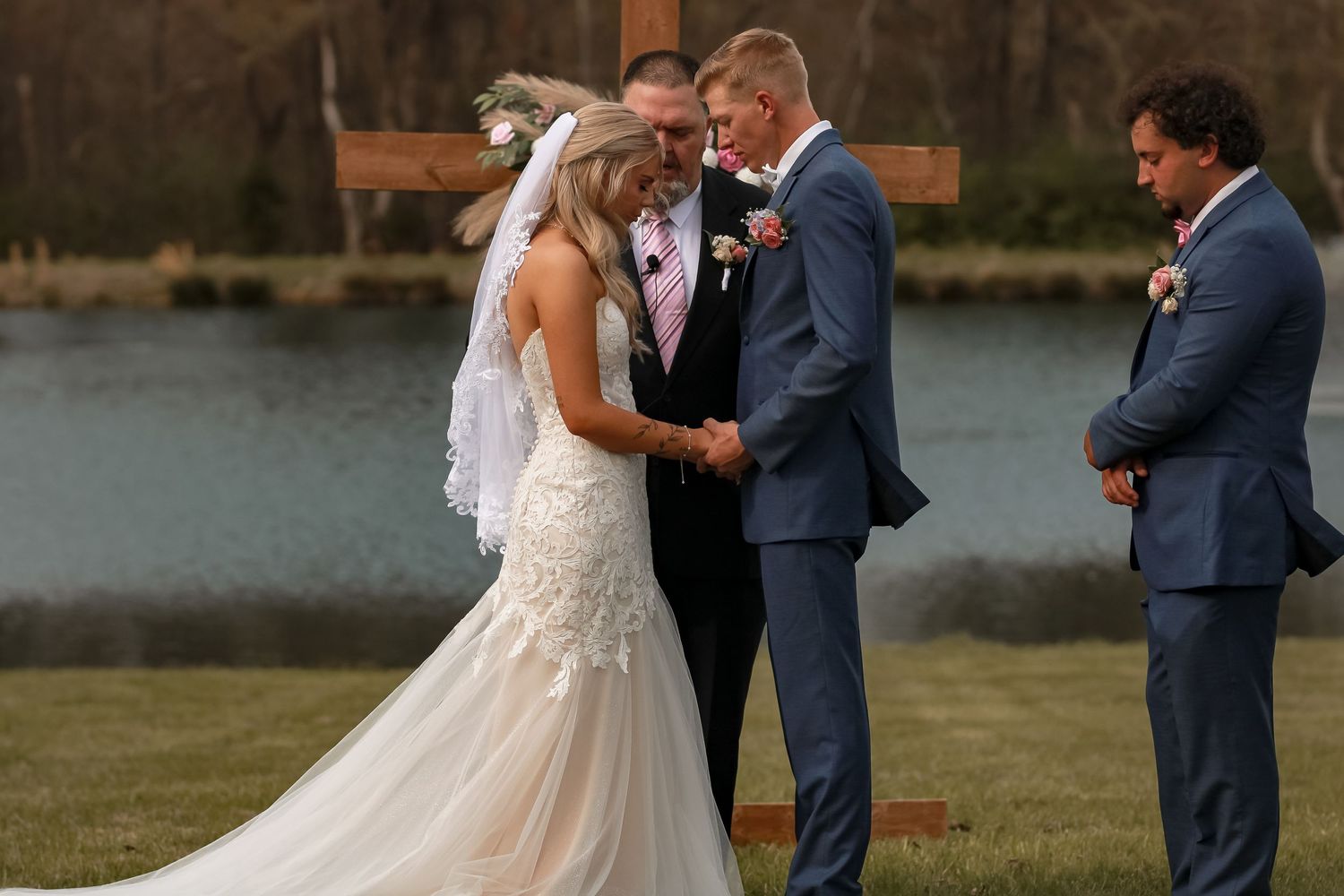 Wedding ceremony taking place outdoors by a serene lake with wooden arch.