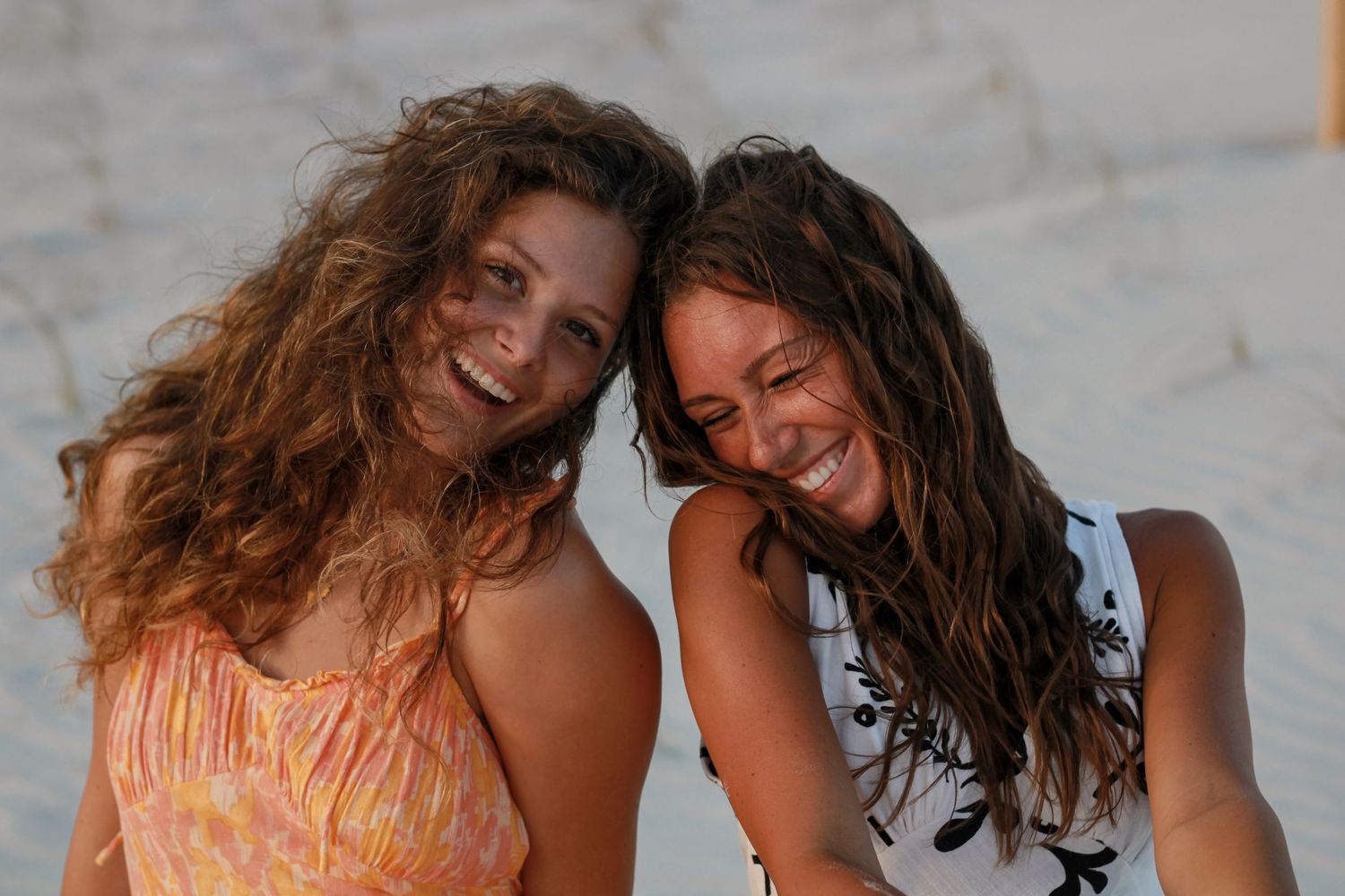 Two friends in colorful sundresses laughing together on a bright sunny day.