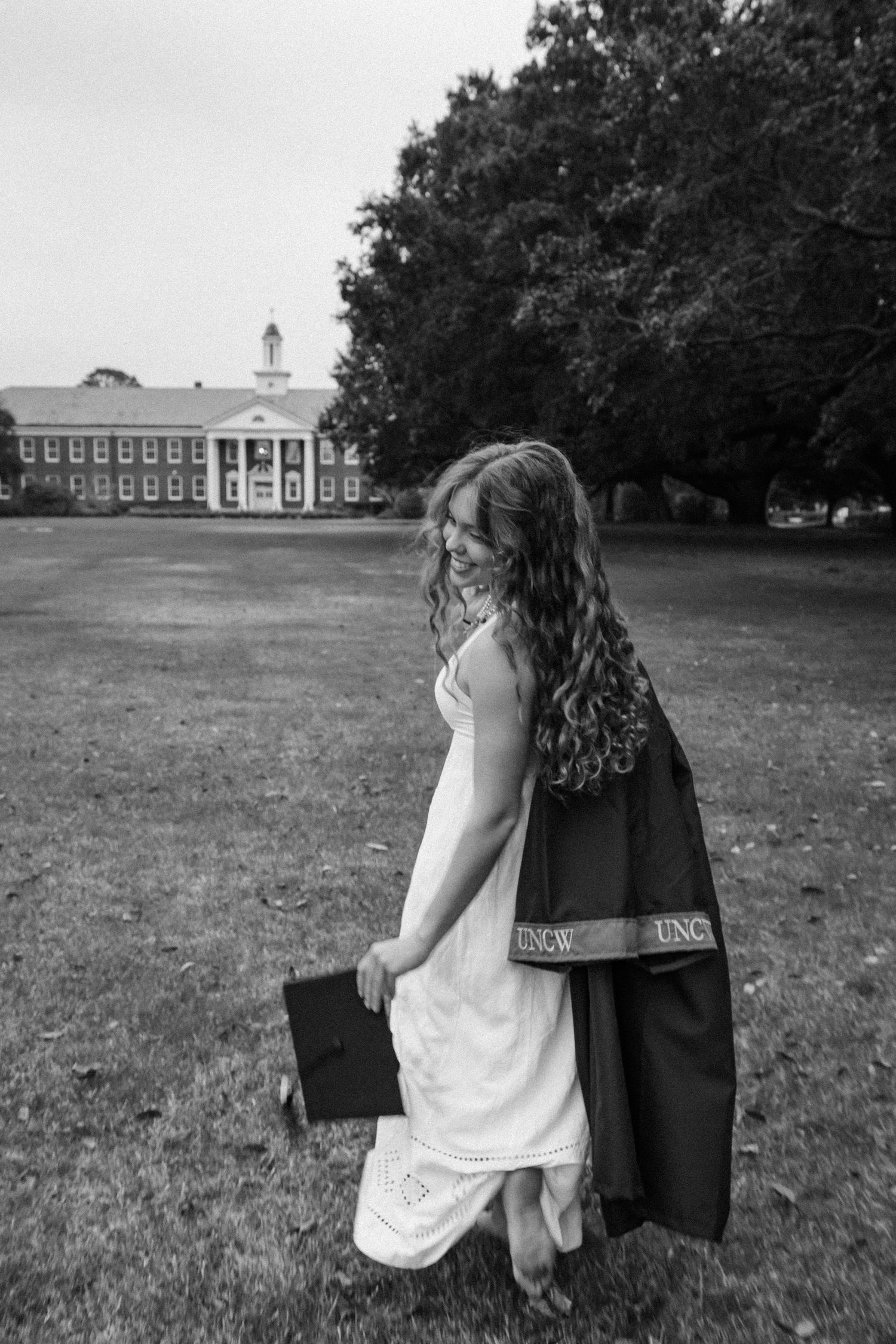 Black and white photo of two people walking together on a grassy field with a building in the distance.
