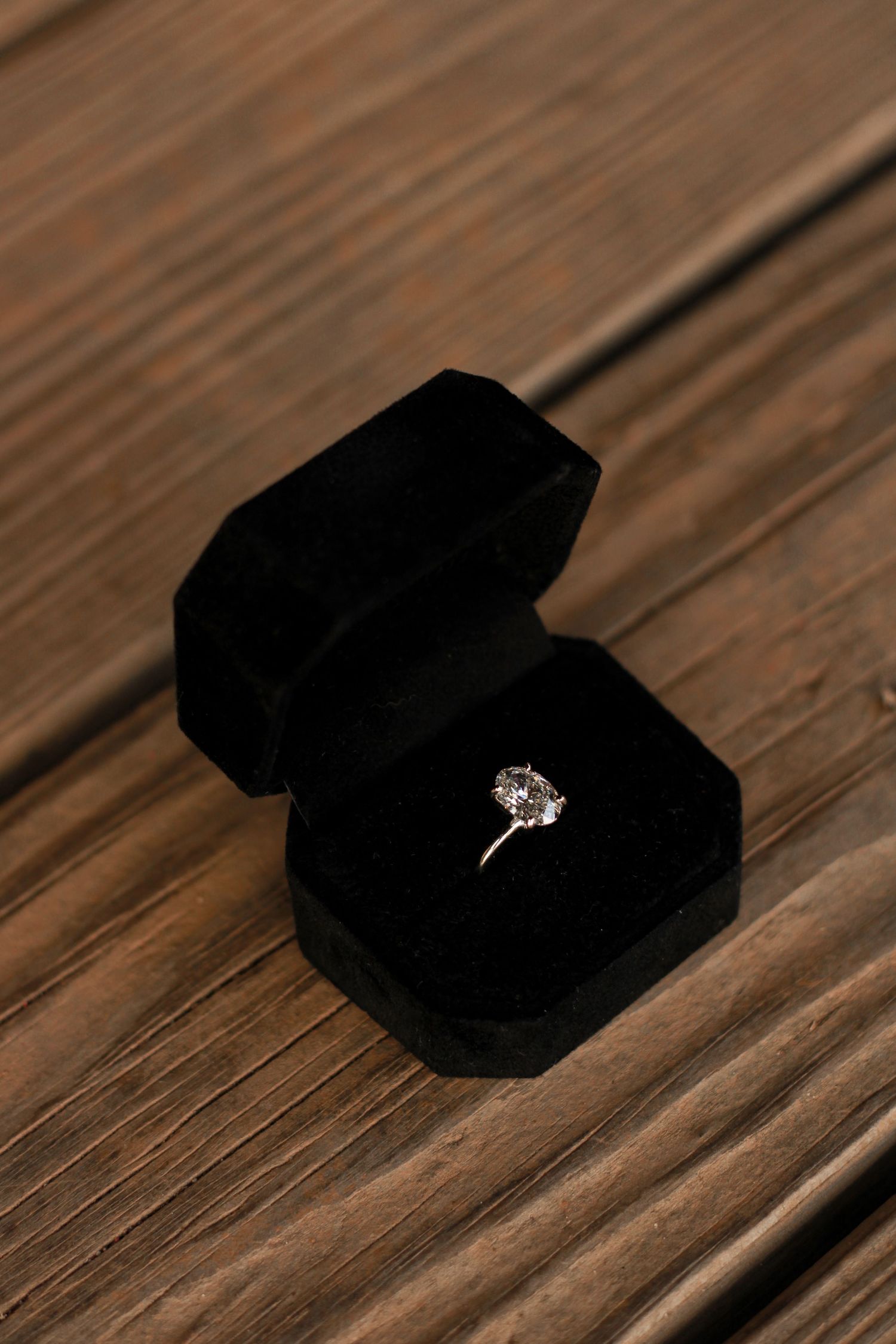 Diamond engagement ring in black velvet box on wooden surface.
