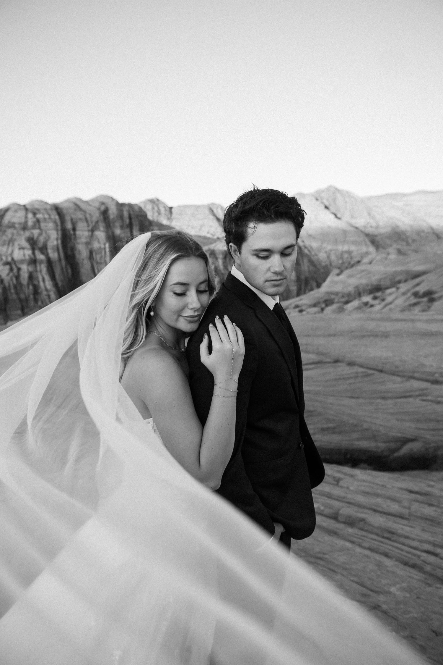Black and white wedding portrait with flowing veil against mountain backdrop.