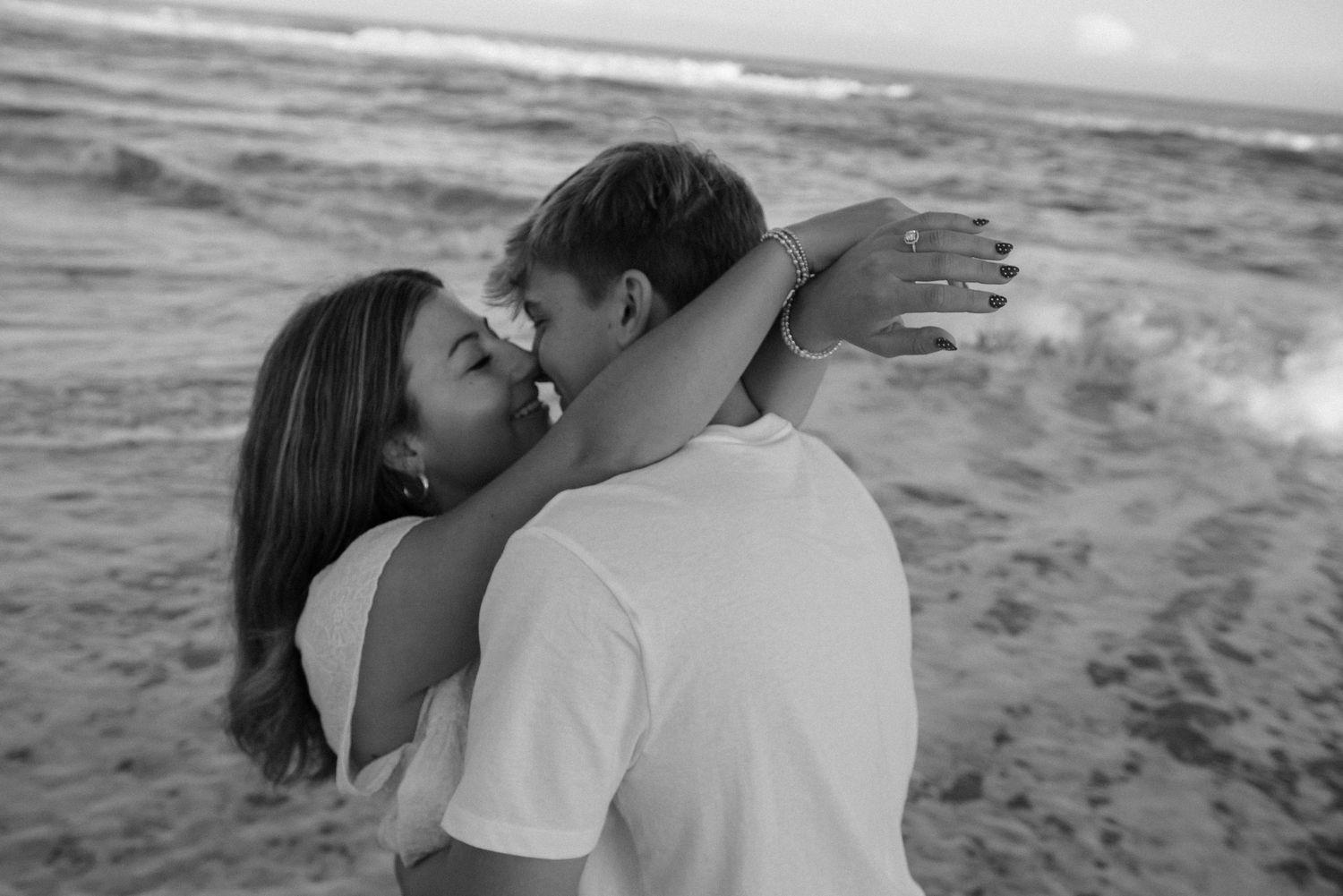 Romantic couple embracing and kissing on a beach at sunset with ocean waves in the background.