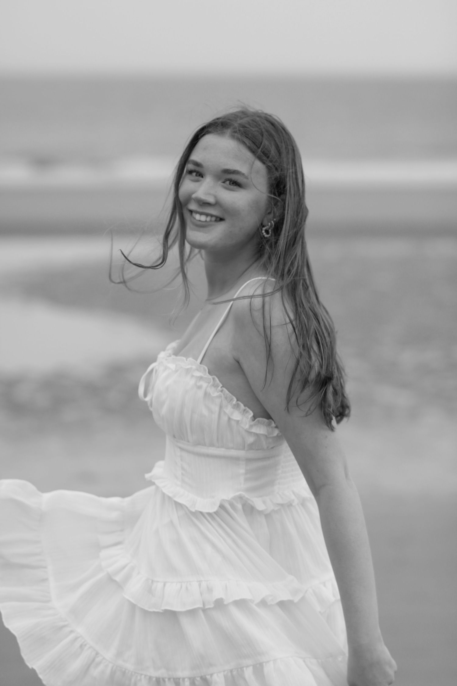 A black and white beach portrait in a flowing white ruffle dress.