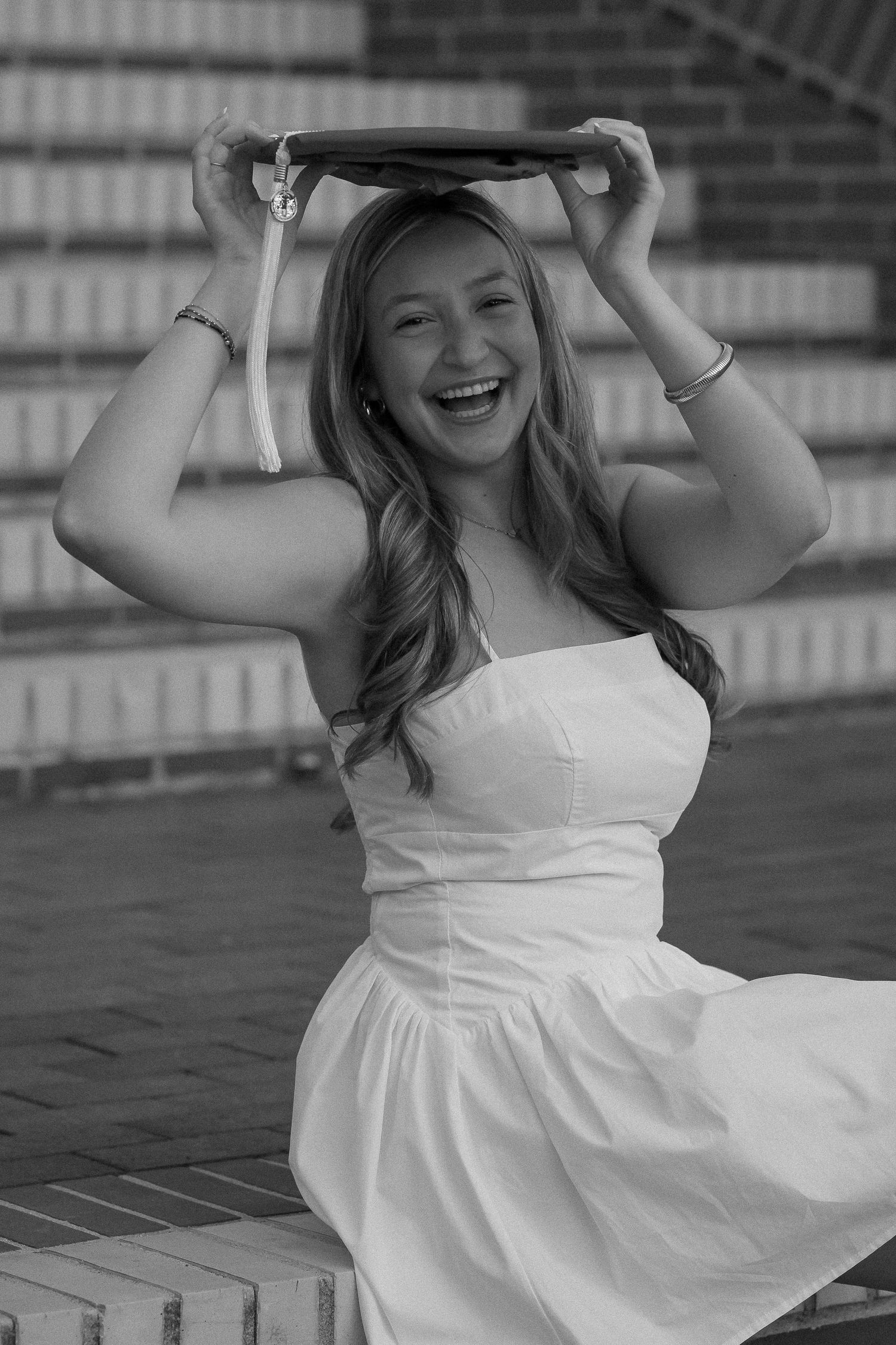Black and white photo of graduate in white dress celebrating on steps.