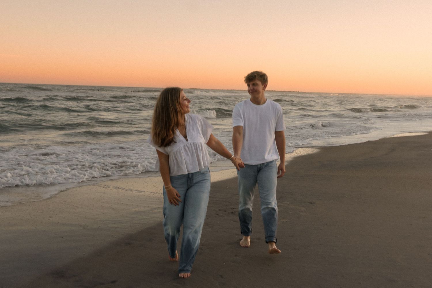 A couple strolling together on a beach with waves in the background.