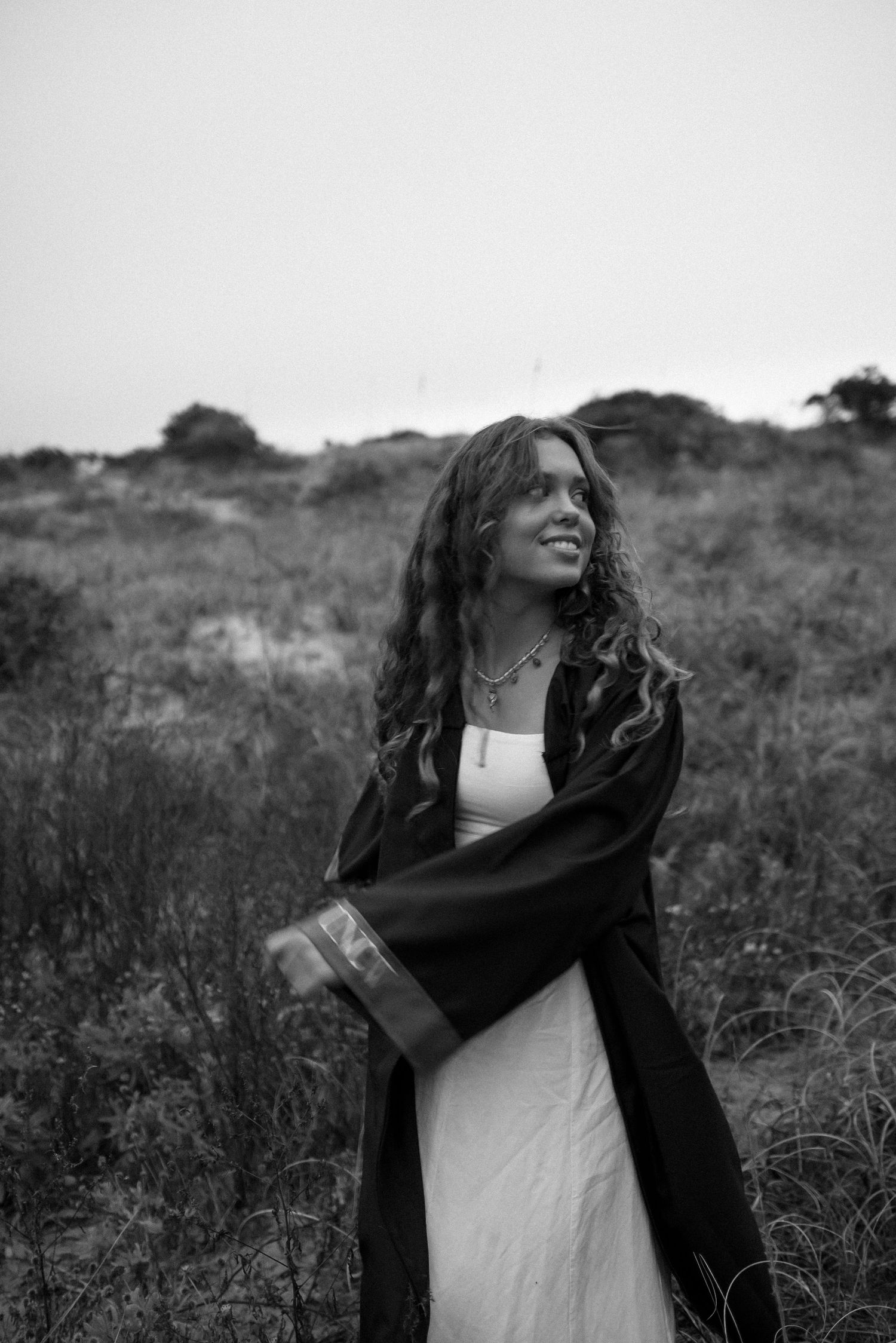 Black and white photos of someone celebrating in a field wearing graduation attire.